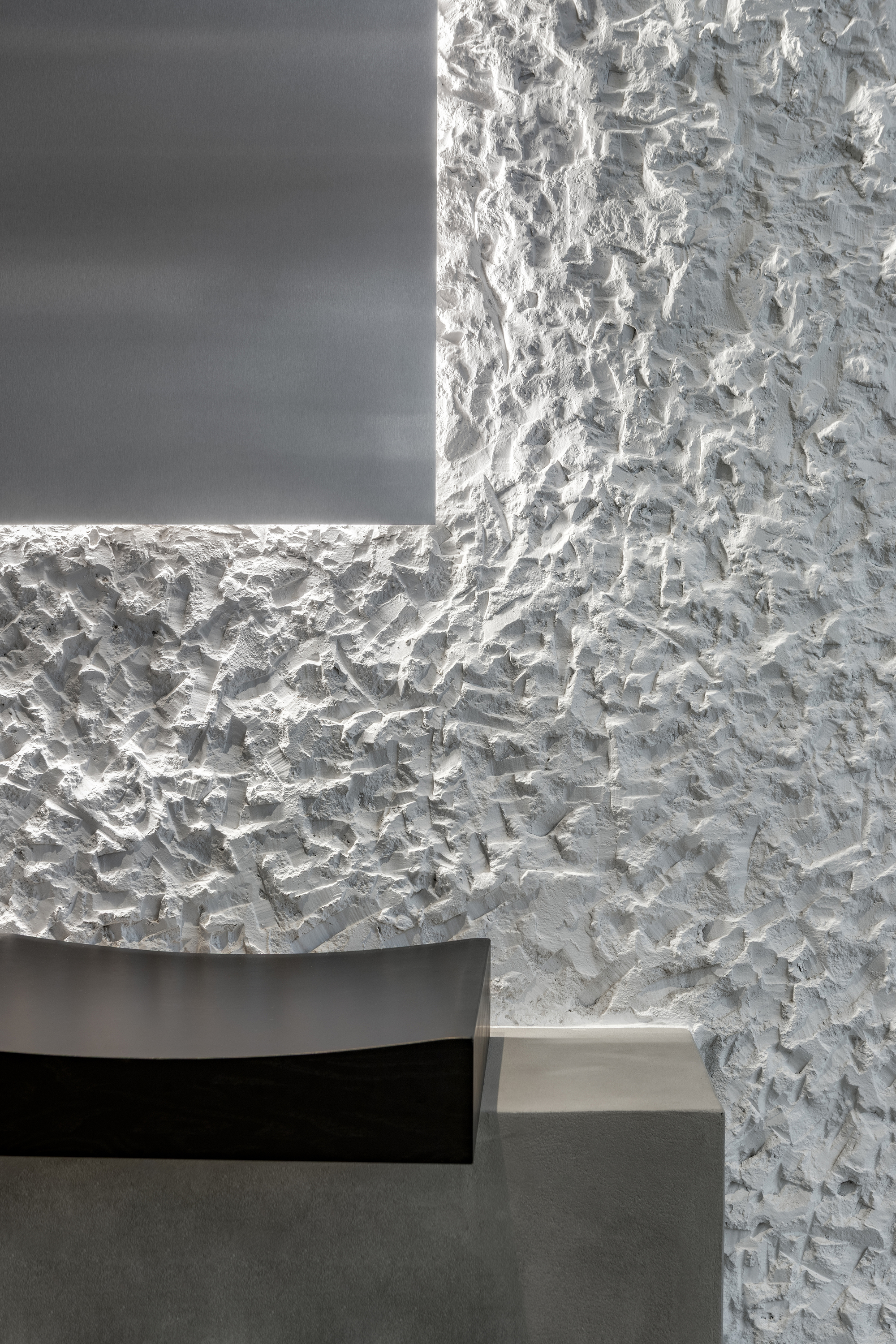 Corner detail where rough white textured plaster meets a recessed dark panel with concealed lighting