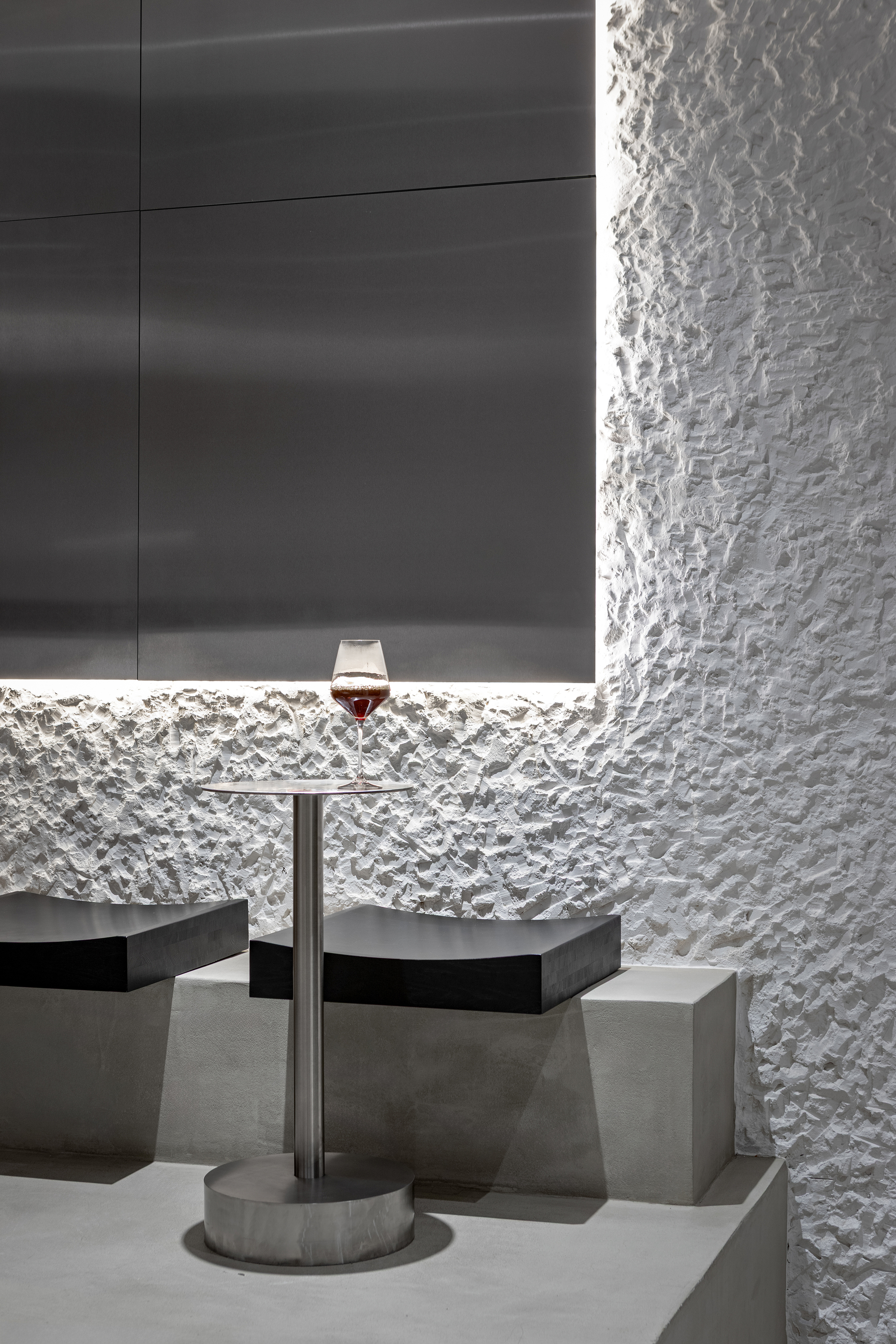 Concrete table with wine glass against textured white wall and backlit horizontal niche