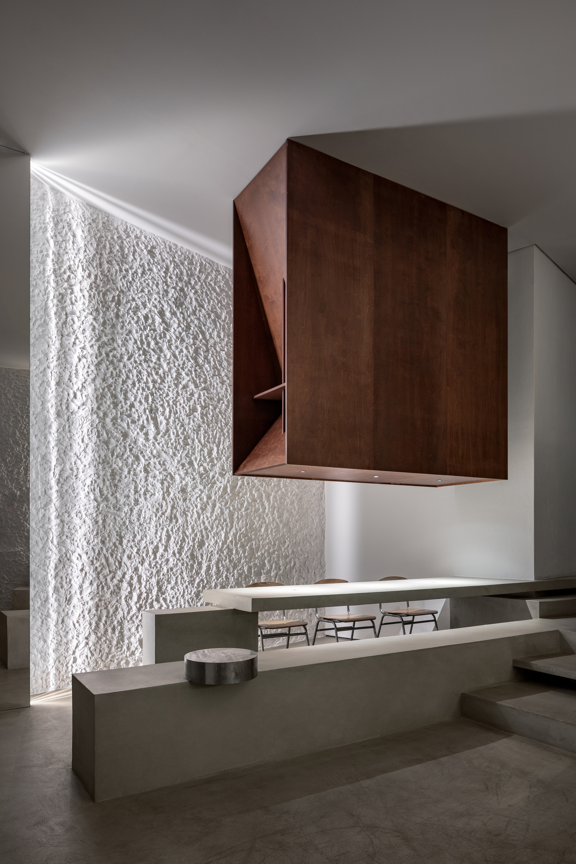 Cantilevered timber volume hovering above concrete counter with textured white wall beyond