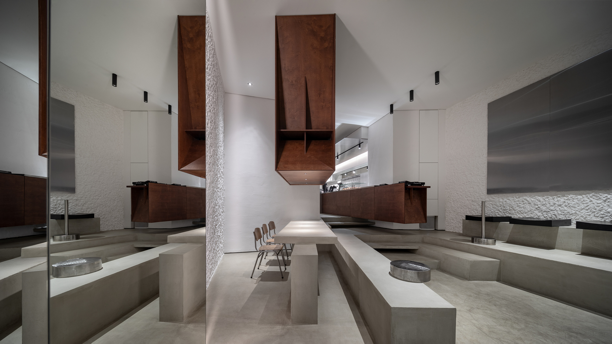 Sunken seating area with concrete benches and walnut cabinetry suspended above a double-height space