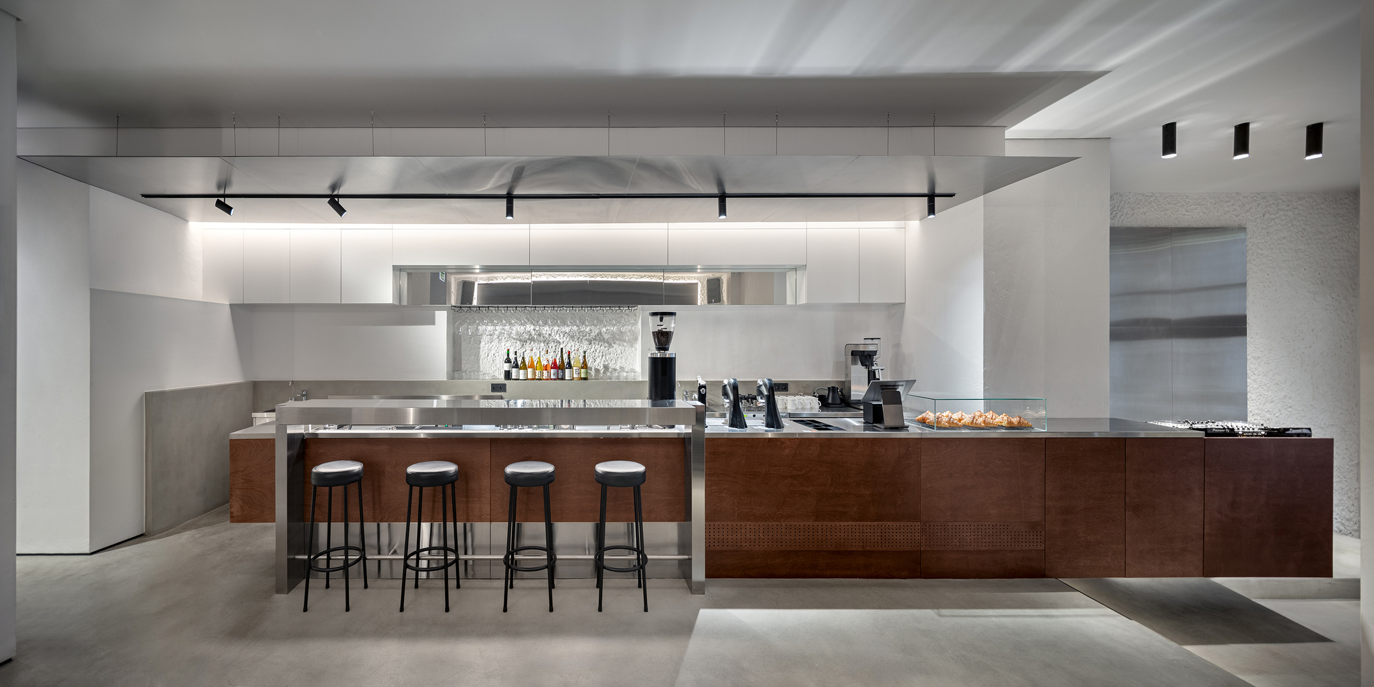 Service counter with walnut base and four bar stools under linear ceiling lighting