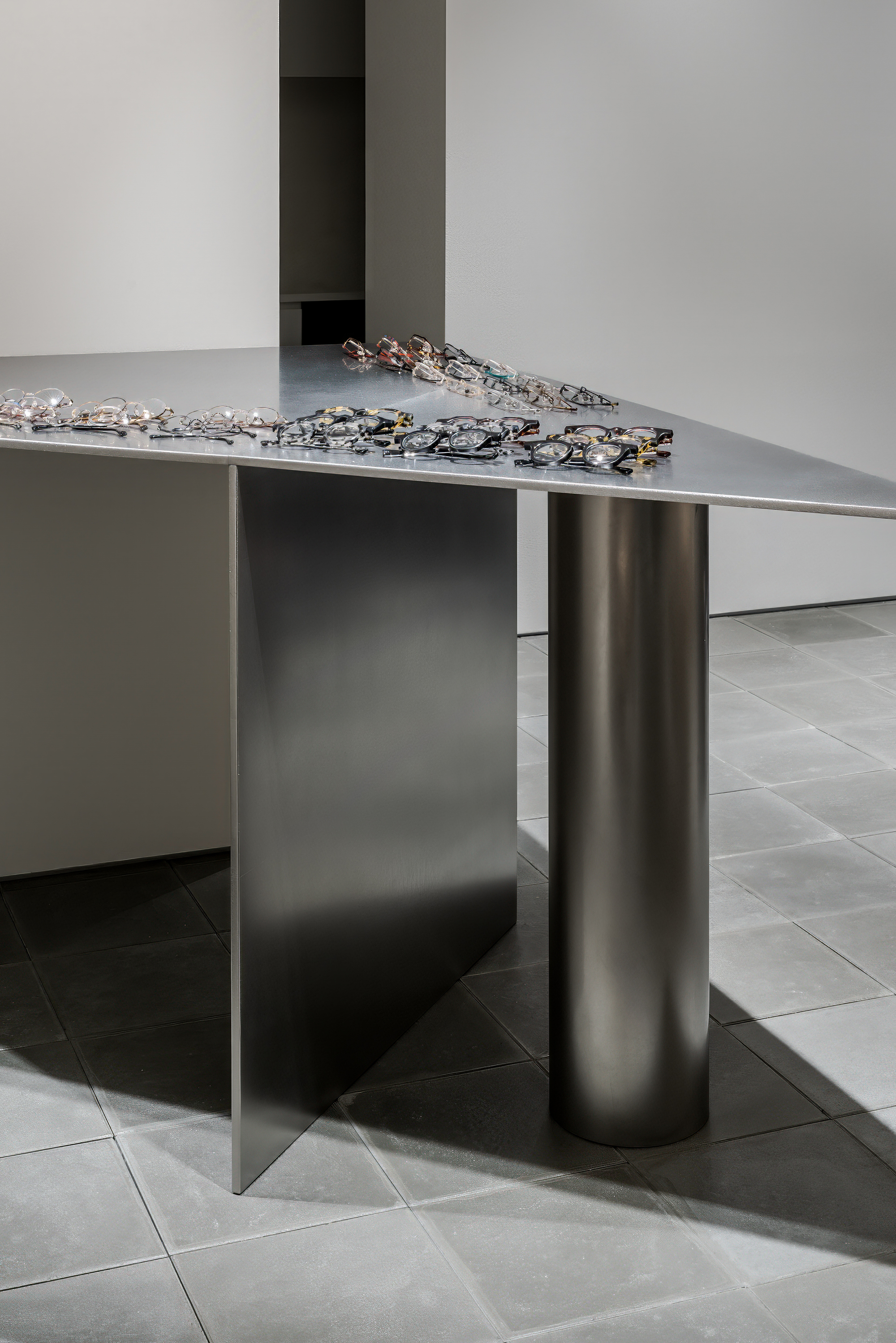Detail of cylindrical steel column supporting a metal display table with eyeglasses