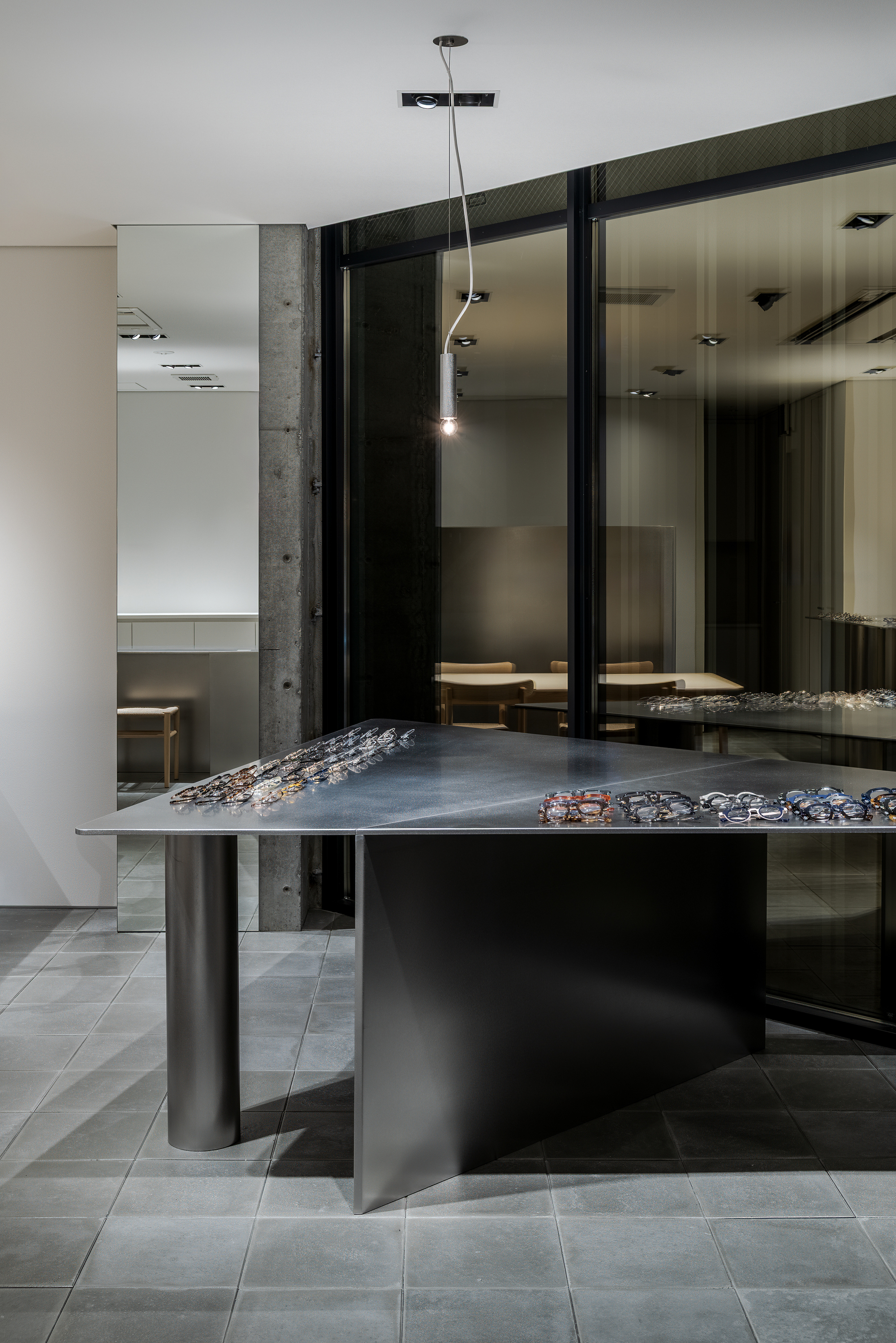 Display table with pendant light above reflecting in dark glass walls behind concrete column