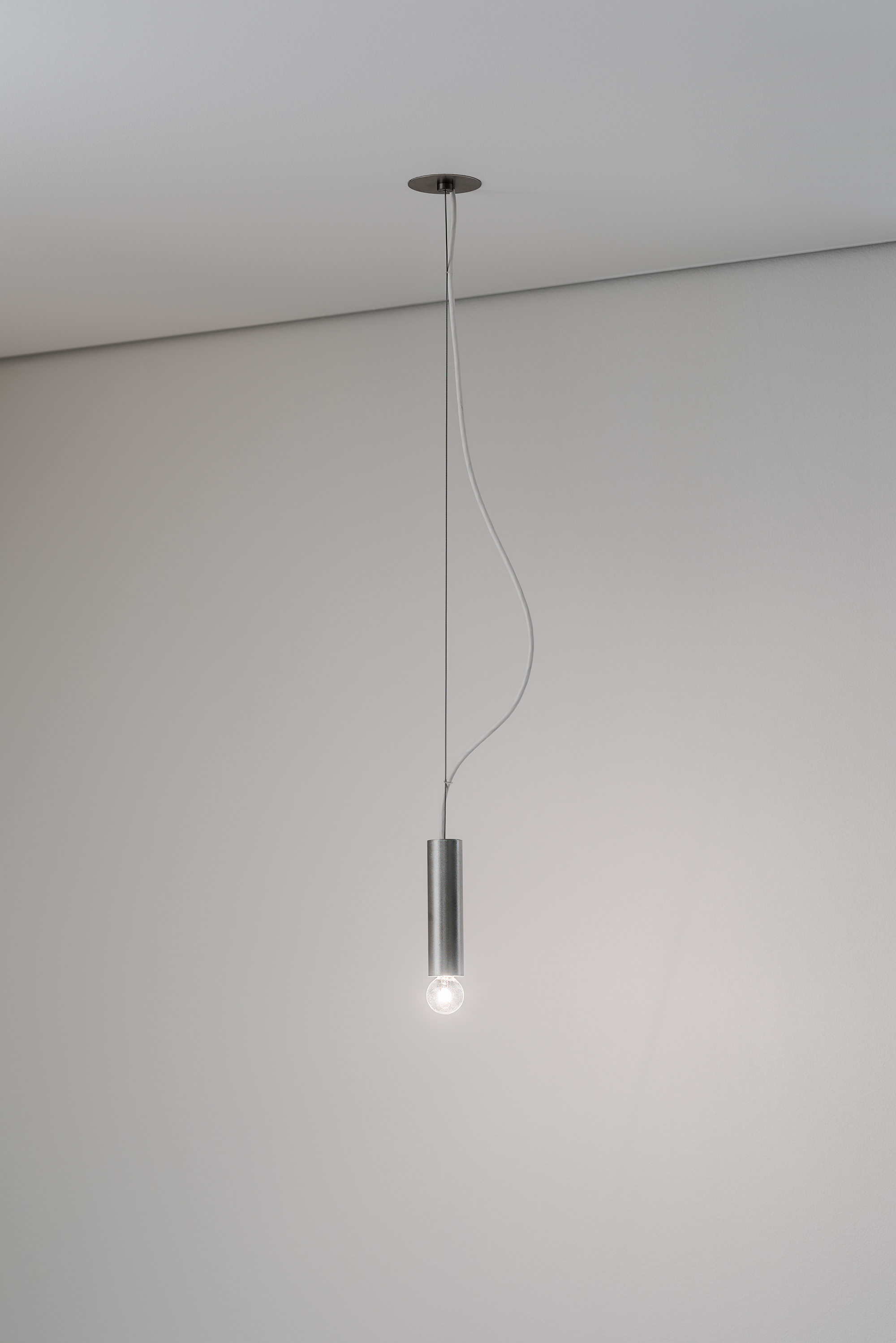 Single pendant light fixture with cylindrical metal shade suspended from ceiling by thin cord