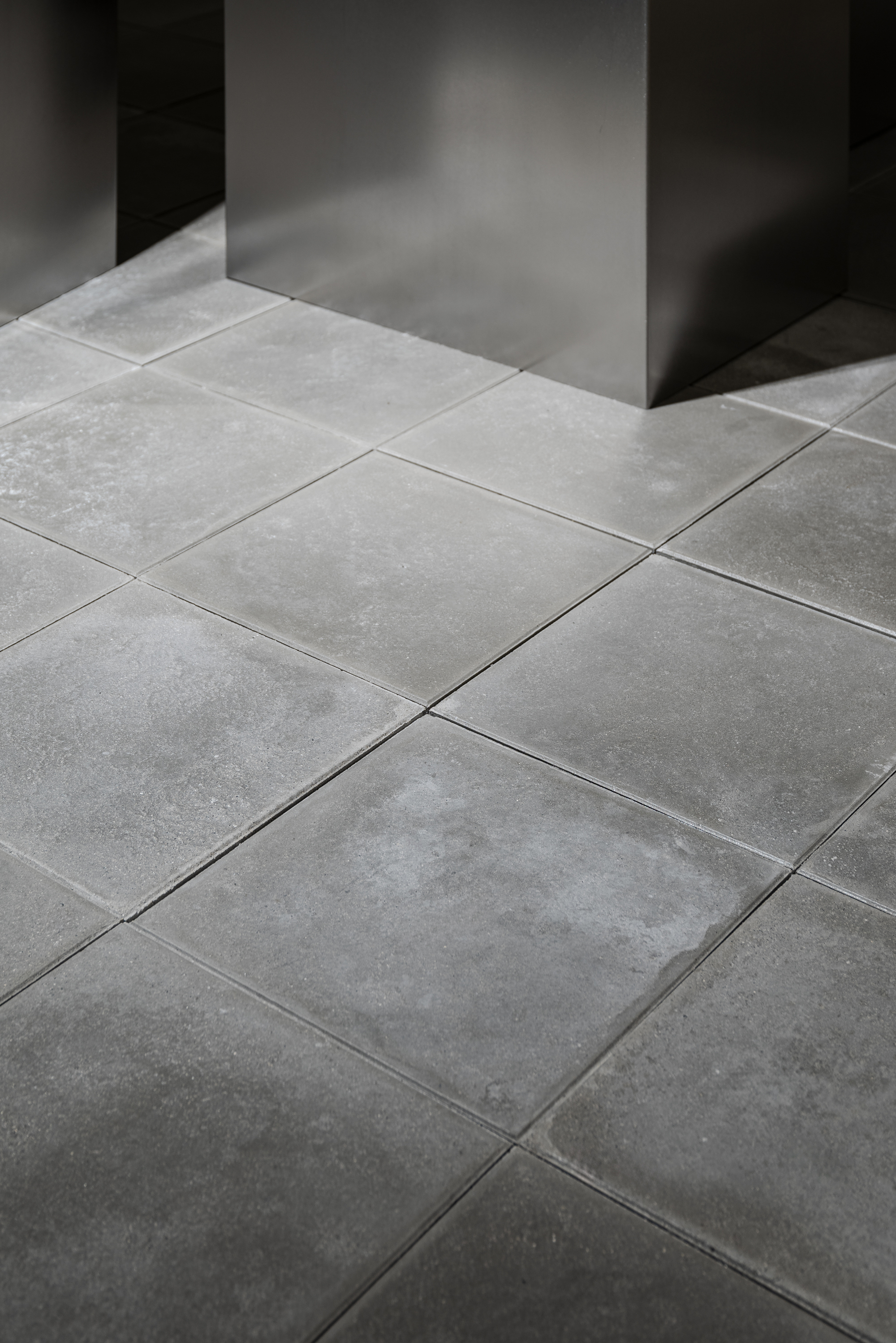 Large format grey stone floor tiles meeting a dark metal column in soft natural light