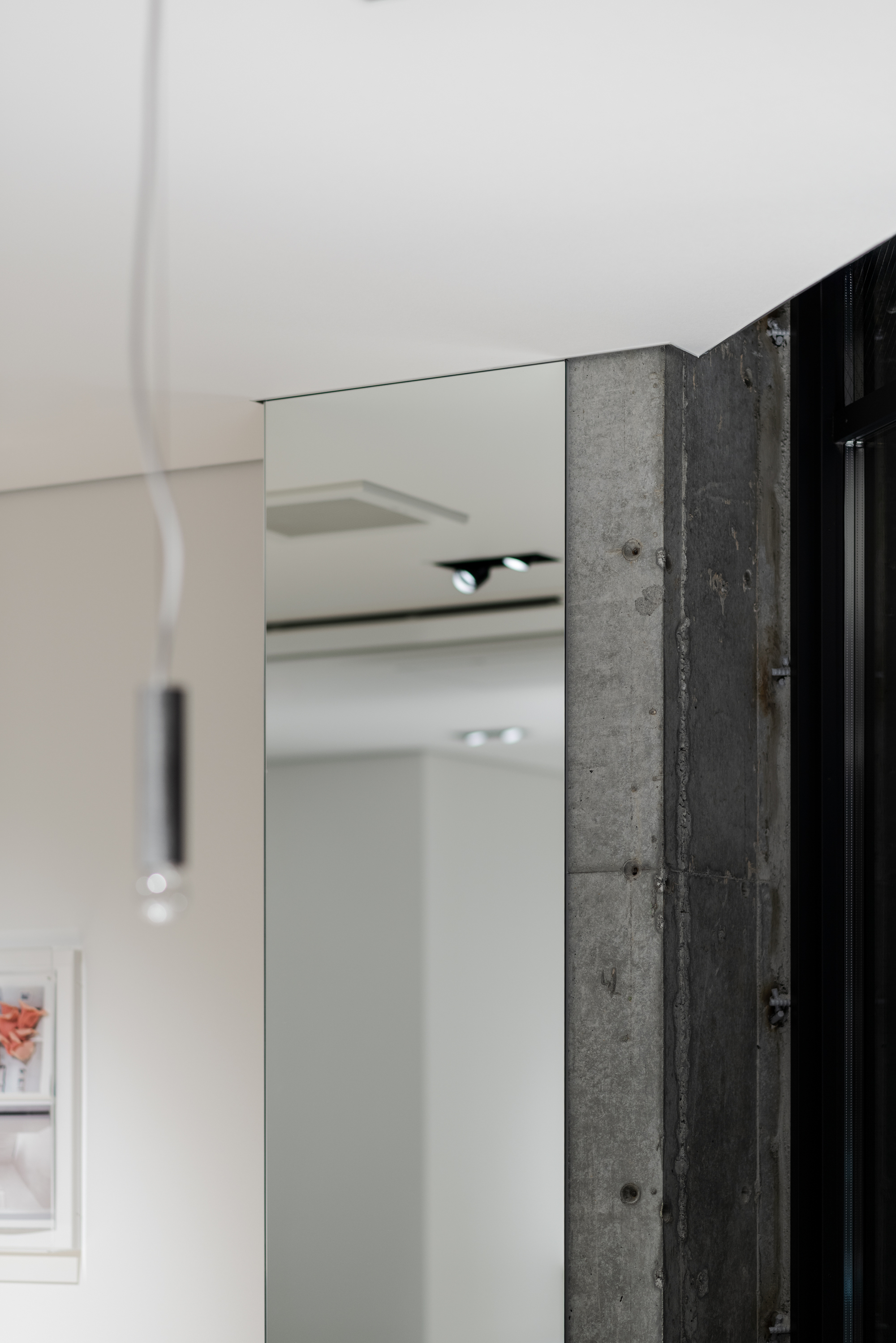 Edge detail where frameless mirror meets exposed concrete column with visible formwork ties