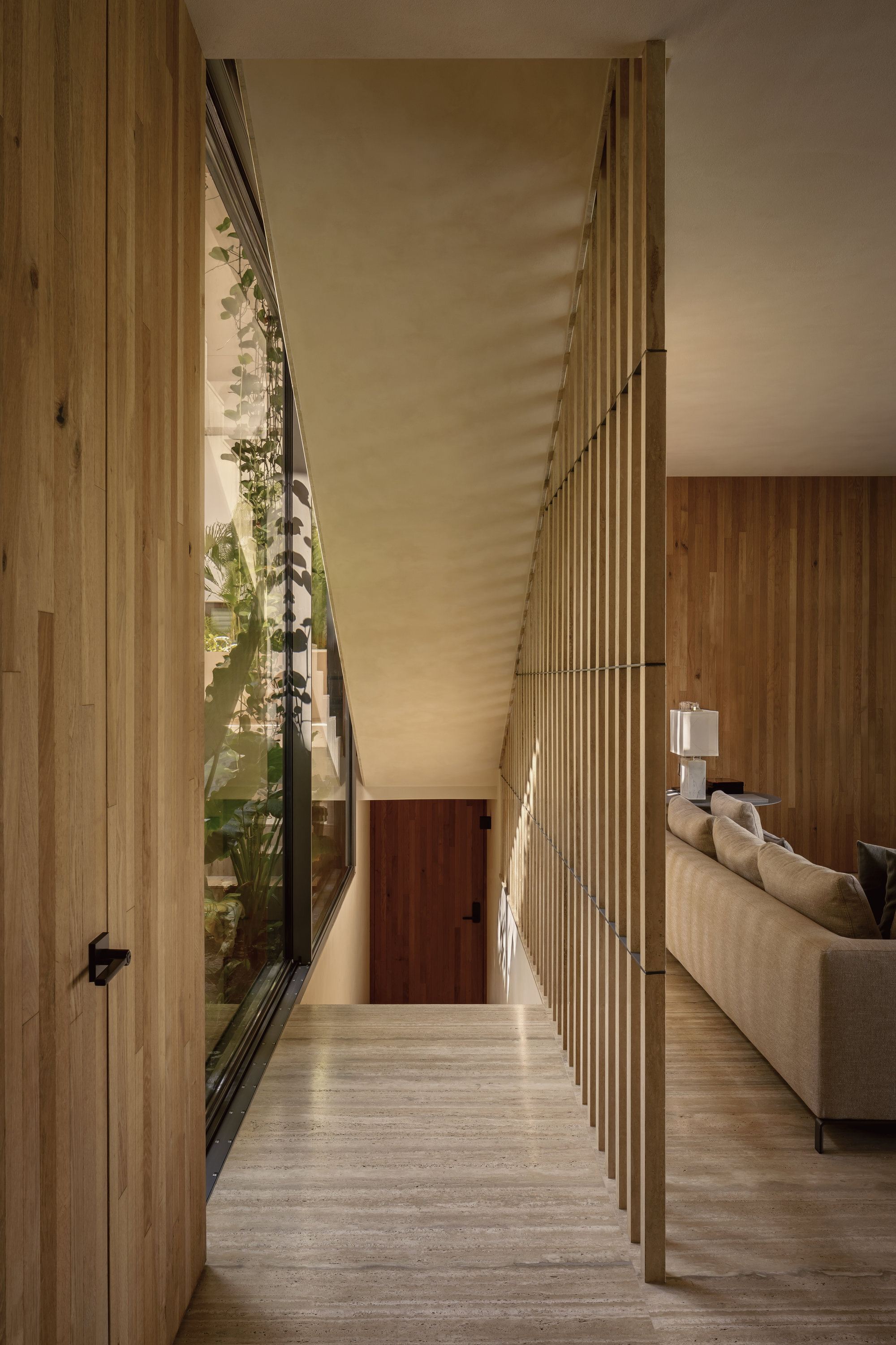 Narrow corridor with vertical wood batten screen and glazed wall opening to planted courtyard