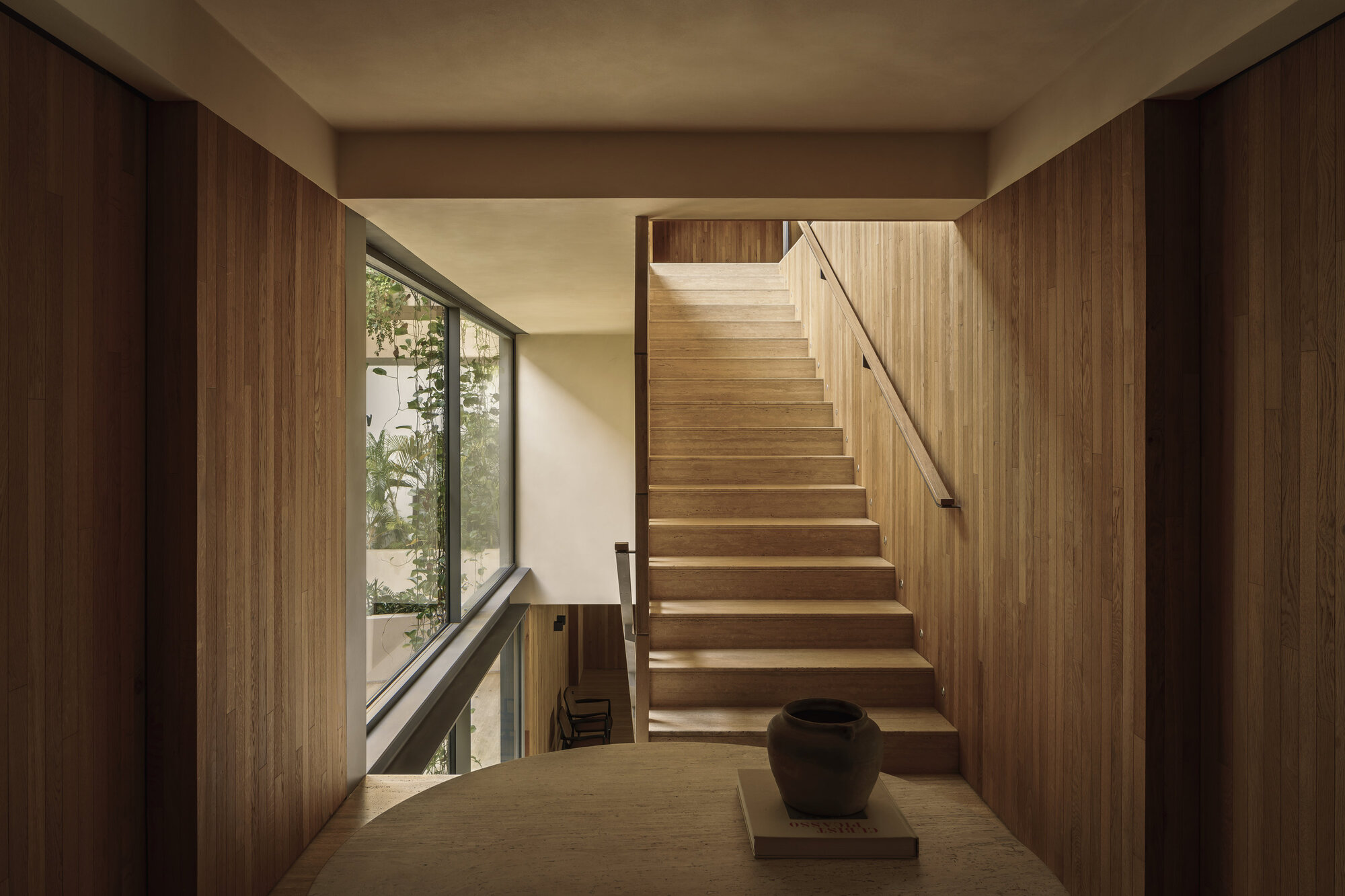 Timber staircase with integrated handrail and slanted window framing greenery outside