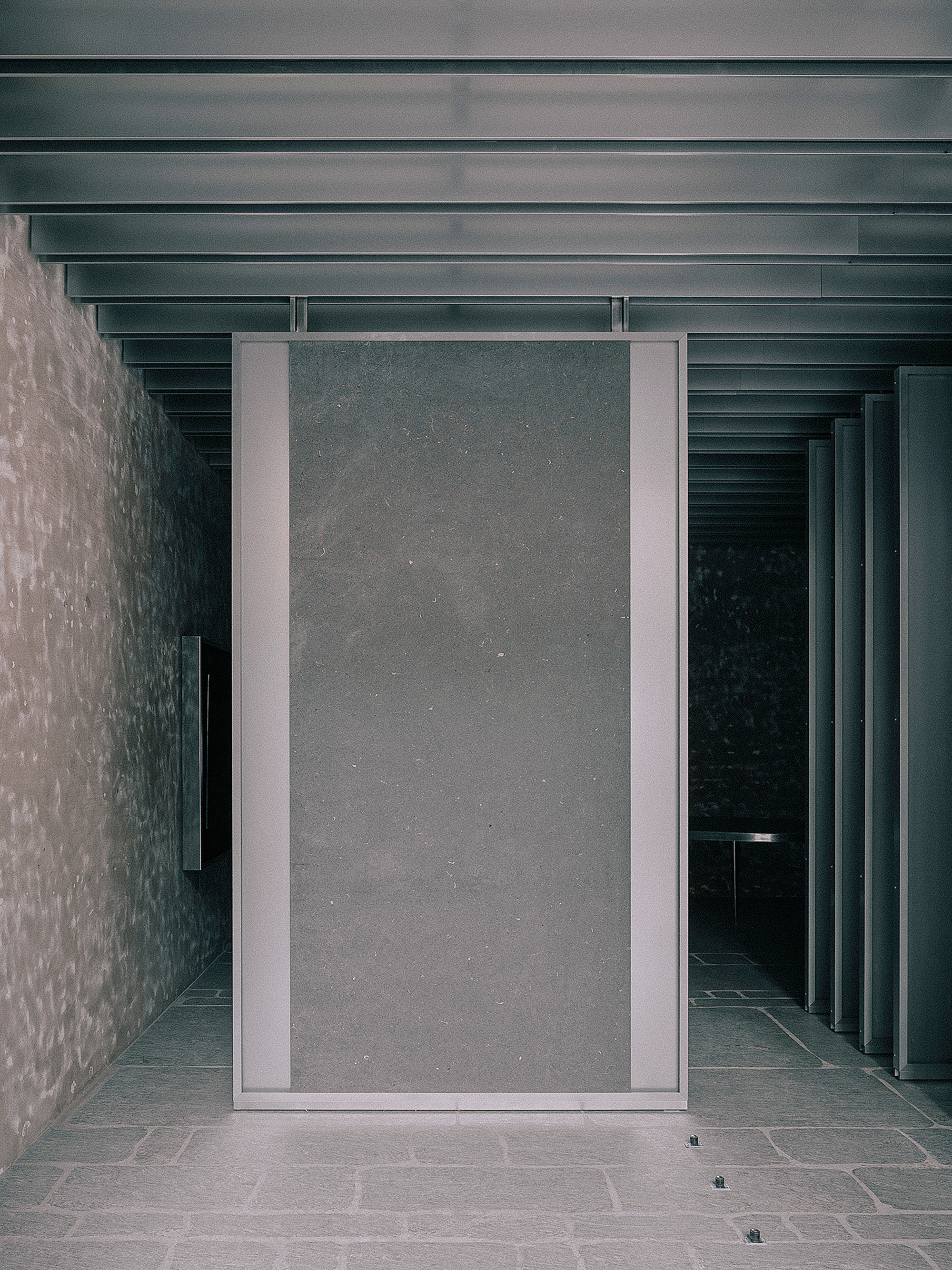 Pivoting metal-framed door panel set between textured concrete walls beneath a ribbed ceiling