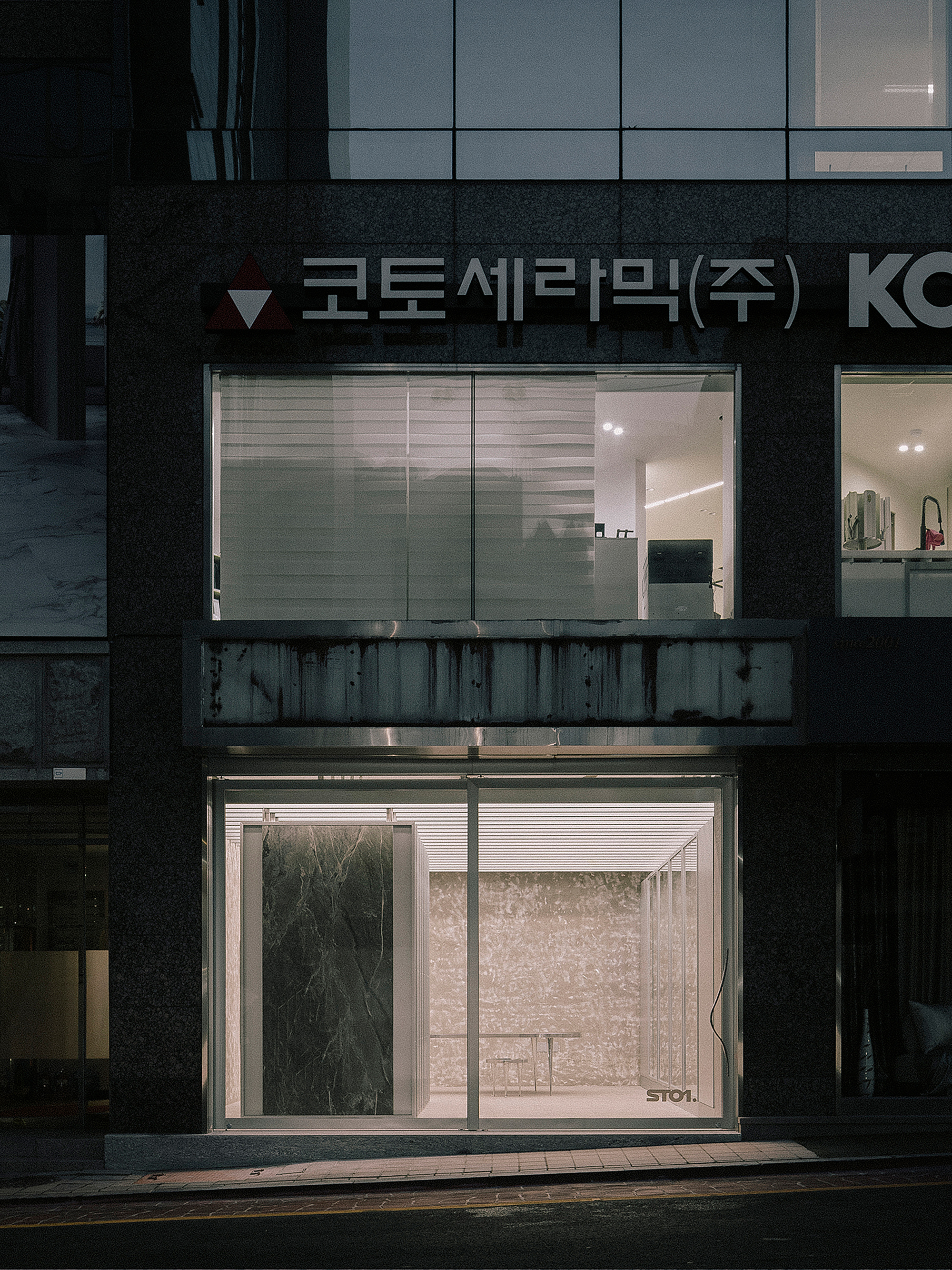 Illuminated storefront with horizontal louvered glass windows in a dark facade at dusk