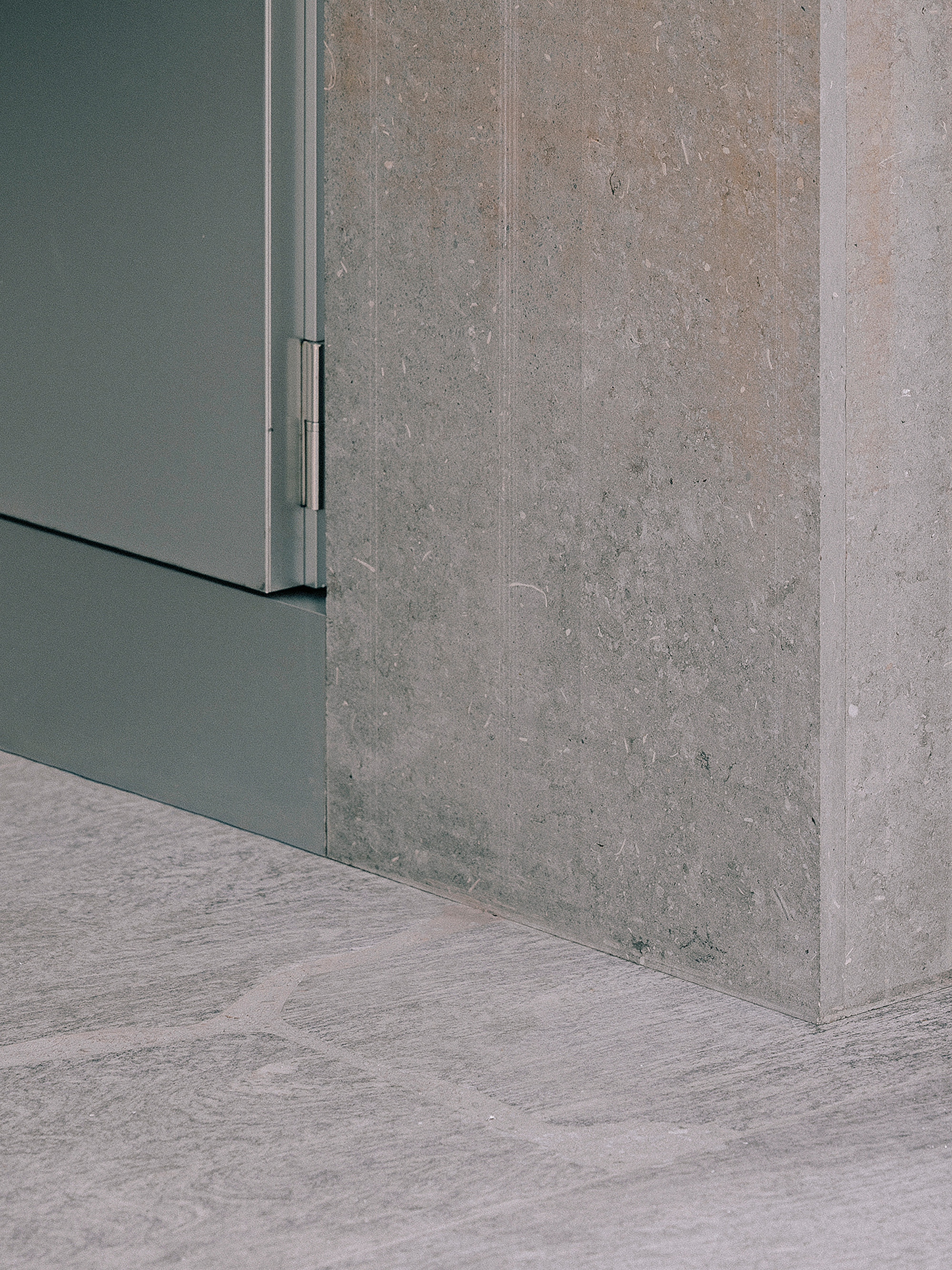 Corner detail where grey metal cabinet meets cast concrete wall and wood flooring