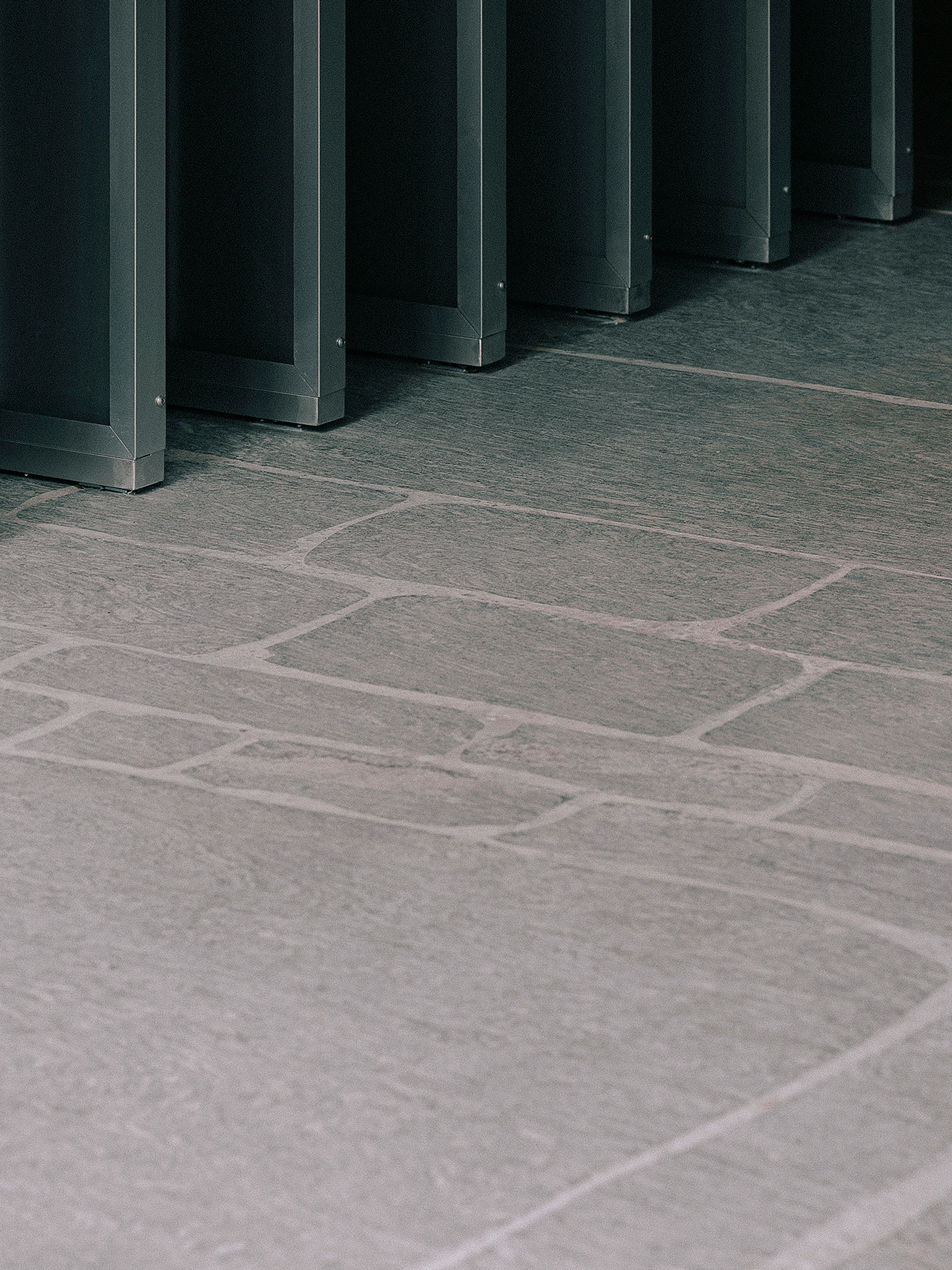 Stone tile floor meeting base of dark metal column framework in low light