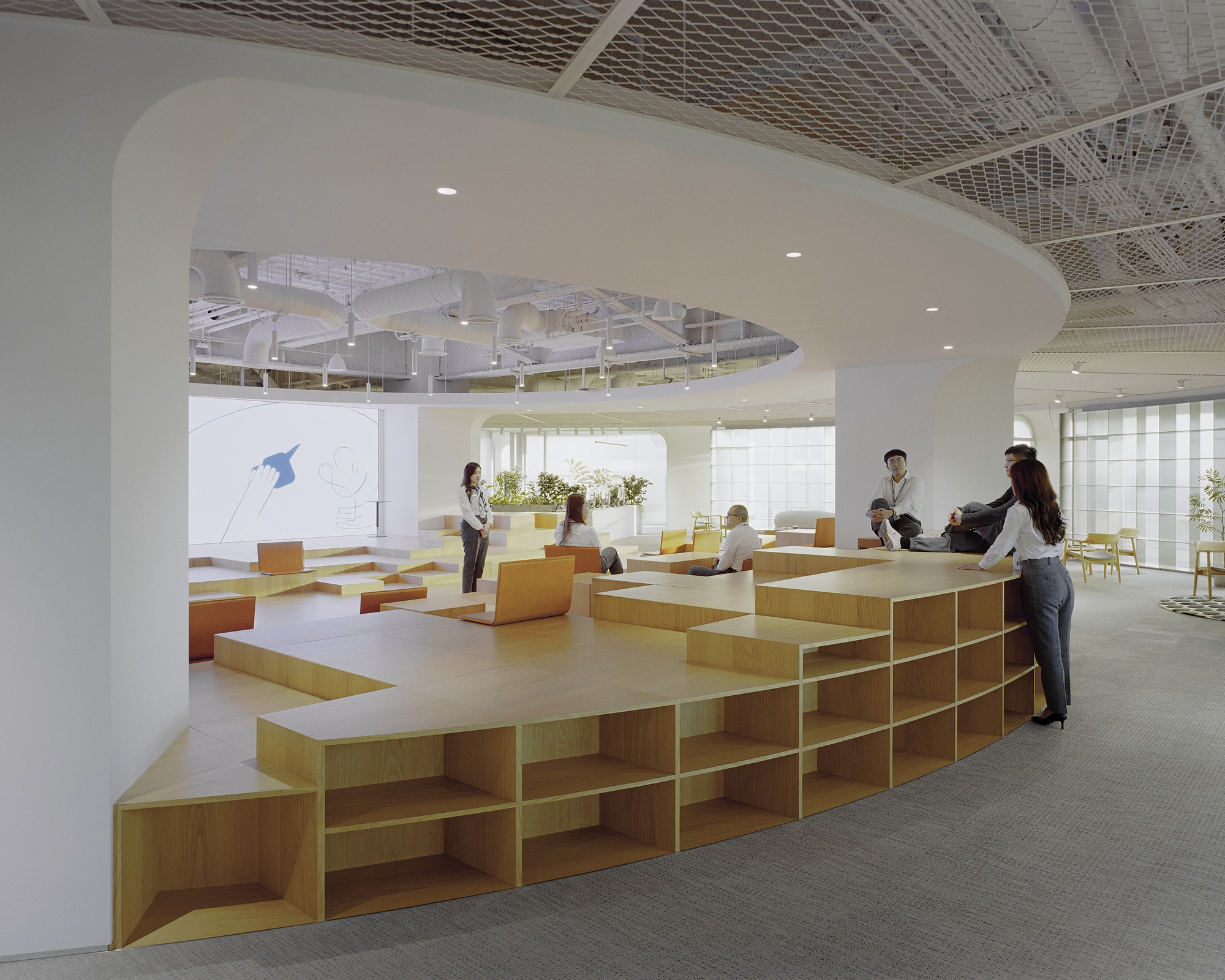 Curved ceiling soffit above modular plywood seating with integrated shelving and people gathered