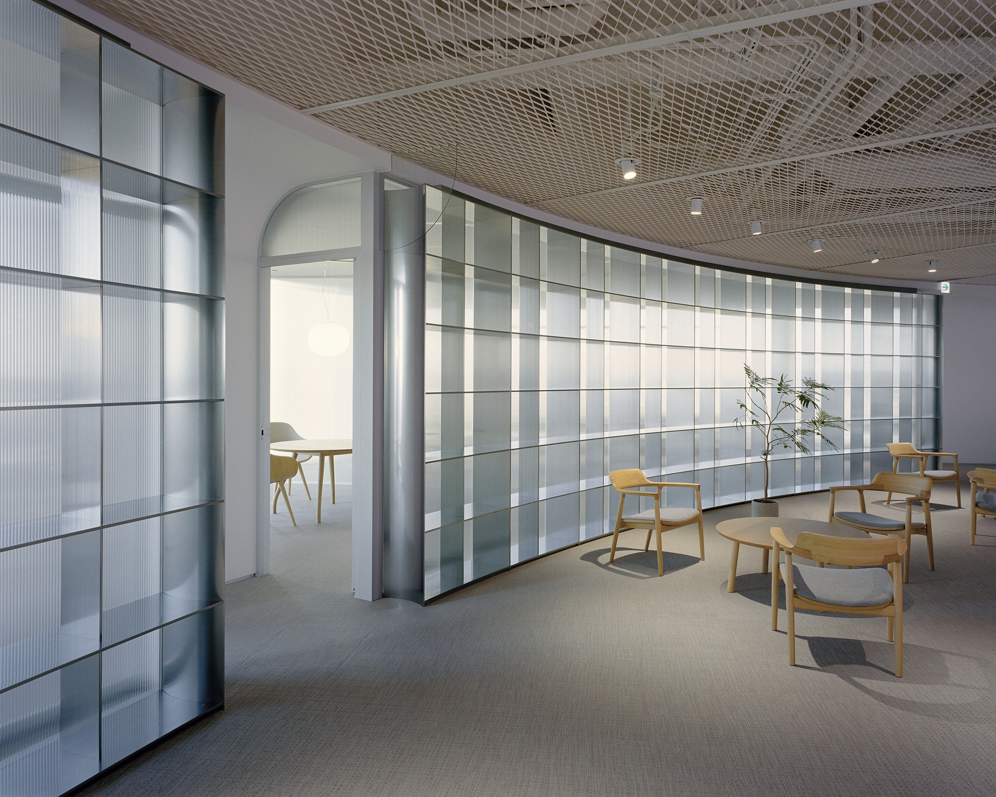 Interior lounge with curved translucent glass panel wall and expanded metal ceiling under recessed lighting