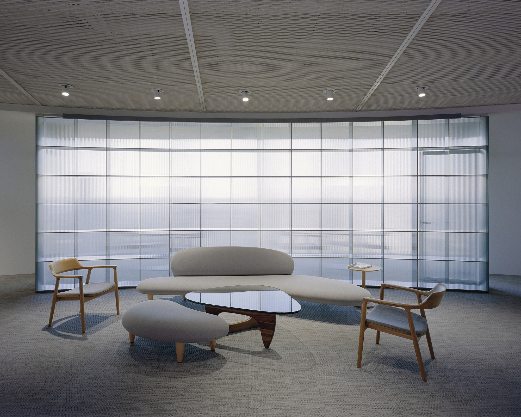 Seating alcove with curved sofa and glass coffee table facing grid patterned translucent facade