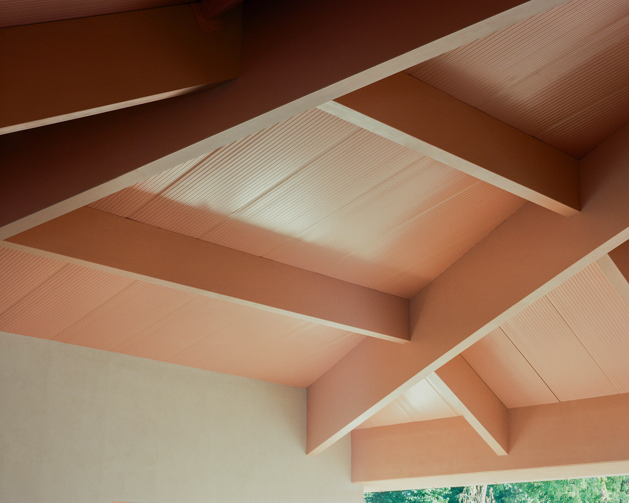Upward view of intersecting gabled ceiling with timber beams and corrugated metal panels in warm light