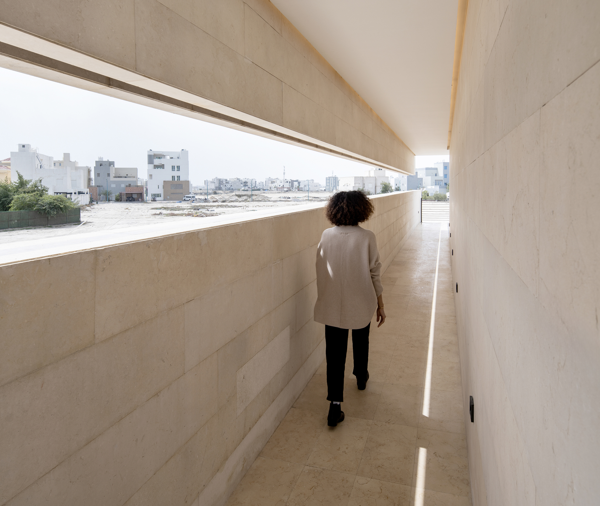 Limestone-clad corridor with horizontal window overlooking the surrounding neighborhood as a person walks toward light