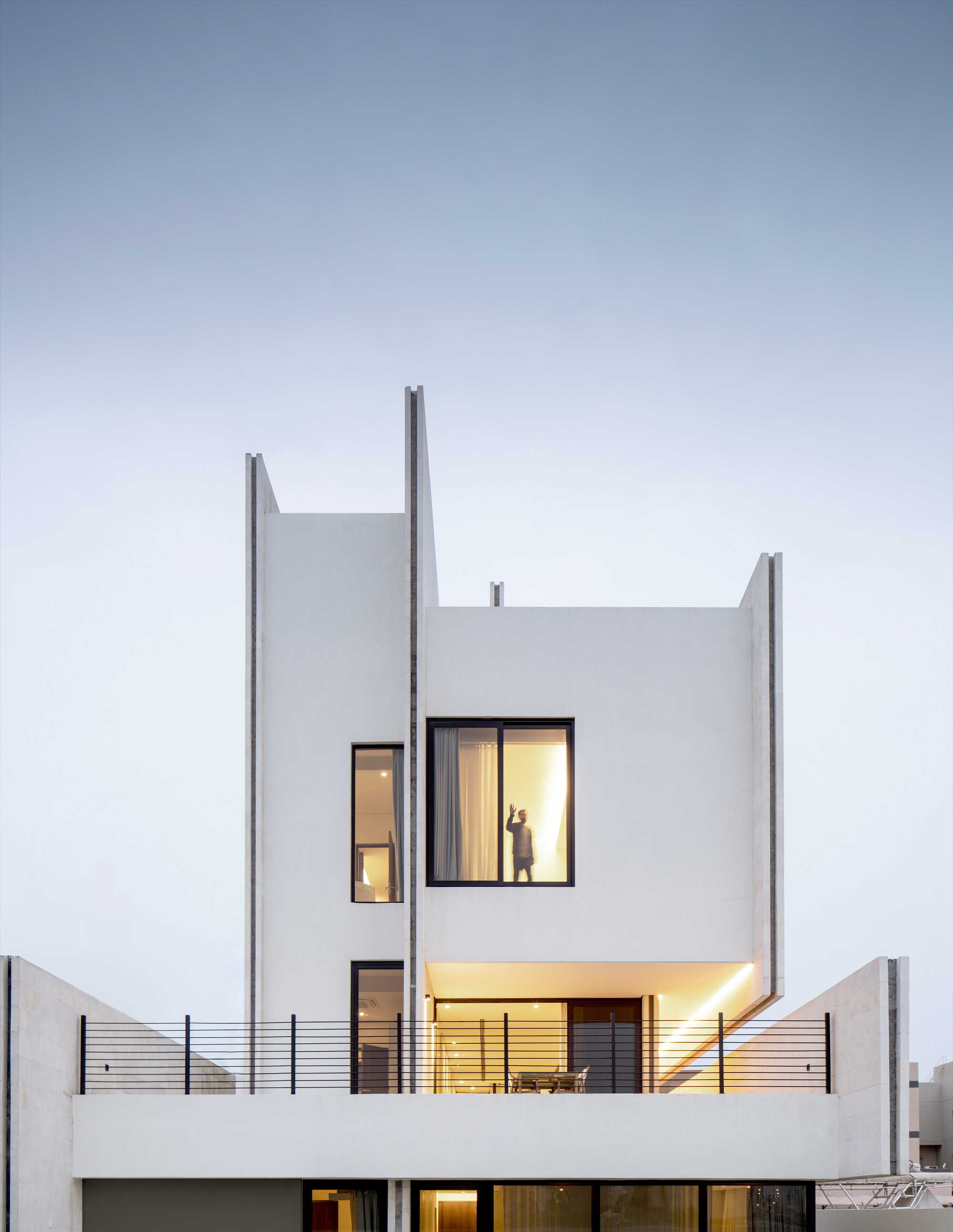 Rear facade at twilight showing illuminated windows and terrace with dining furniture behind horizontal wire railings