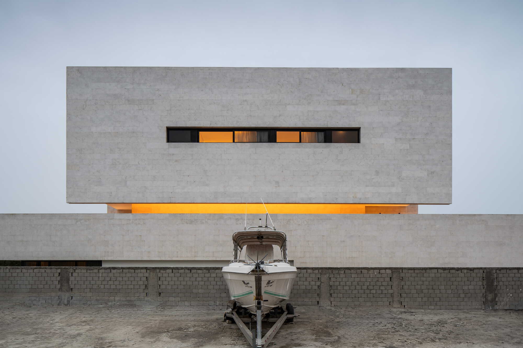 Street facade with horizontal ribbon window glowing at dusk and small boat parked on trailer below