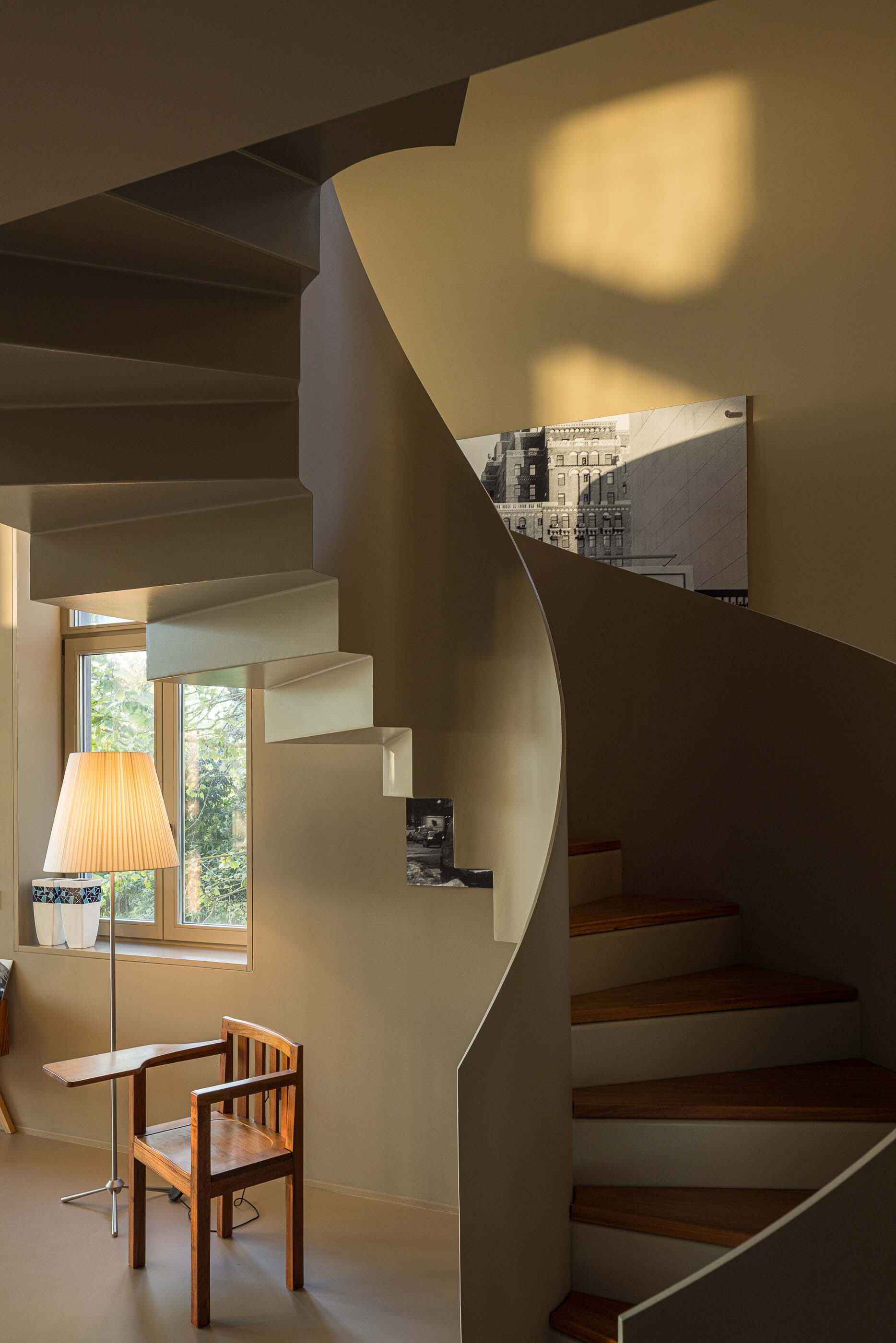 Spiraling stairwell with cantilevered treads and white plaster walls illuminated by afternoon light