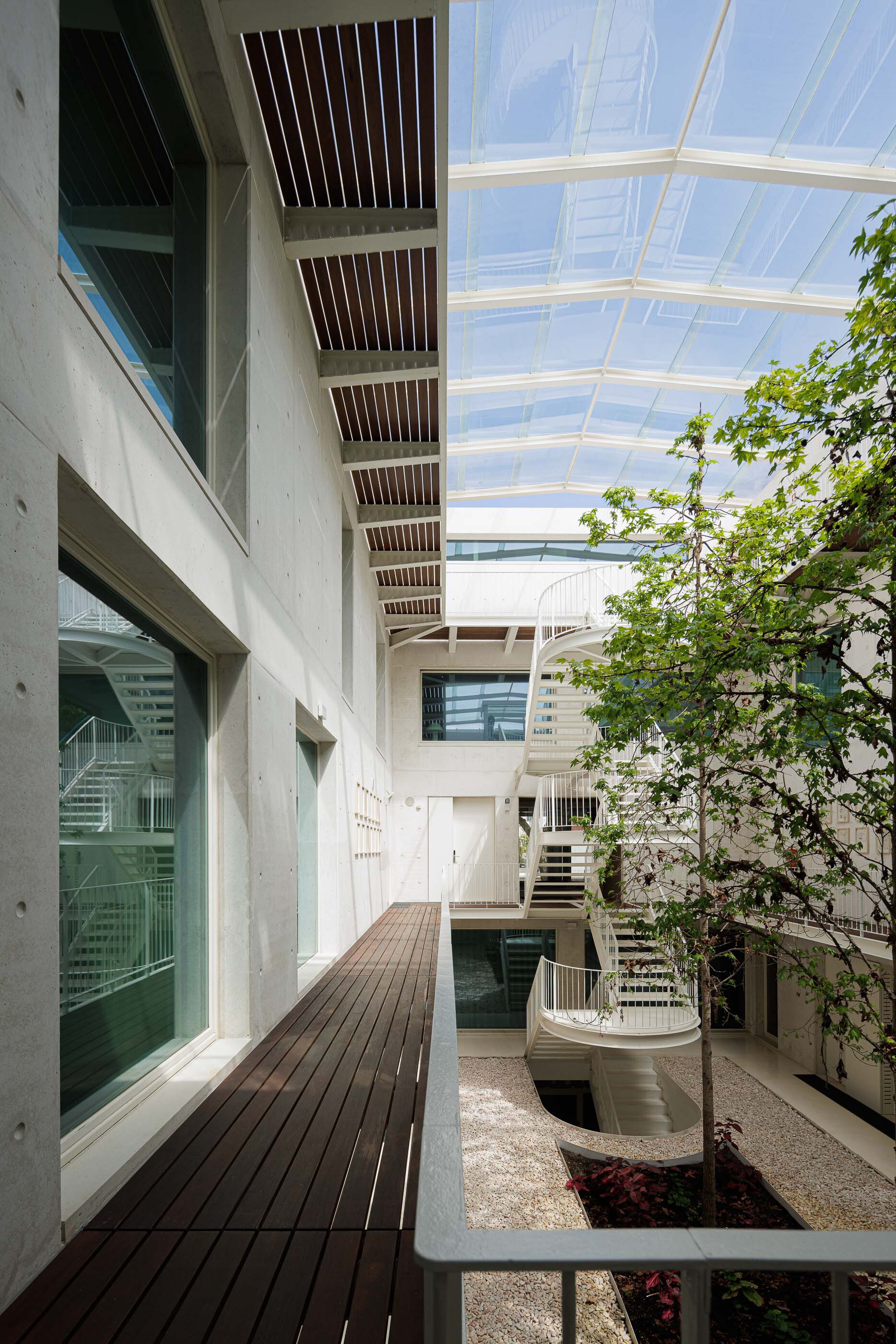 Internal courtyard with curved spiral stairs and planted beds beneath a glazed roof on a sunny day