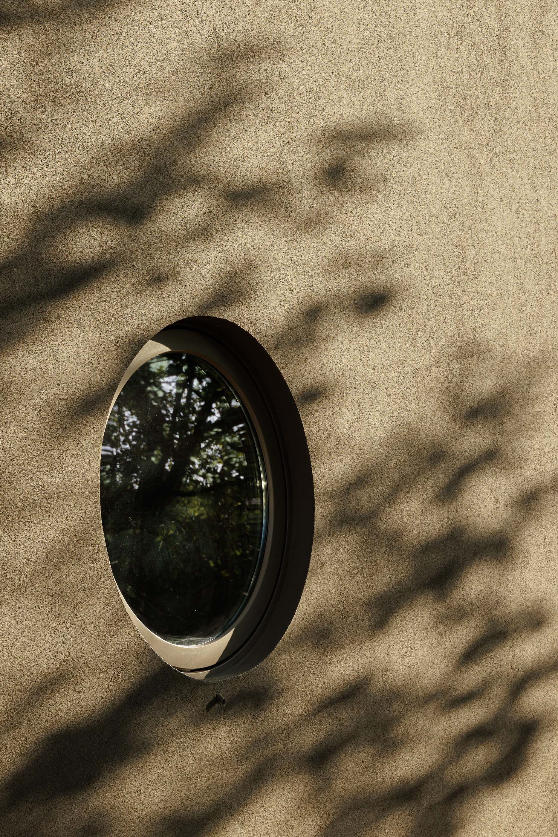 Circular window set in concrete wall with tree shadows cast across the surface
