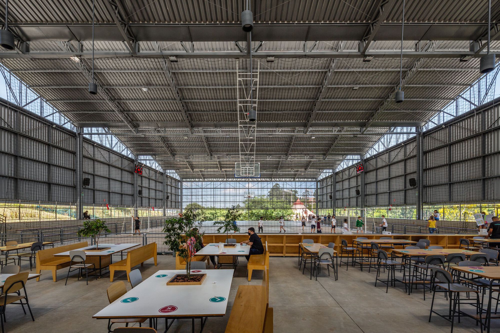 Communal seating zone with timber furniture under industrial ceiling and translucent mesh screens flanking glass walls