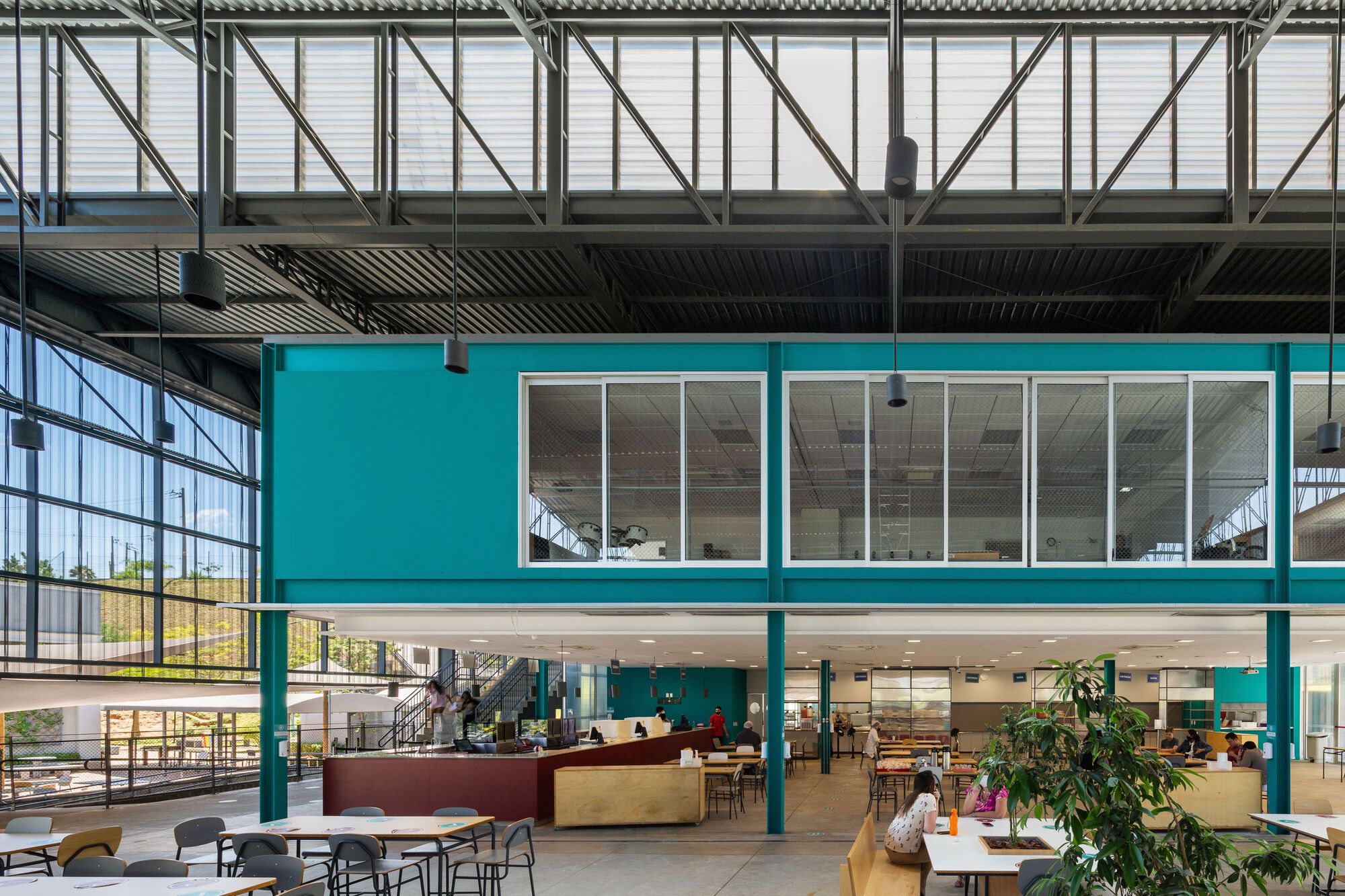 Turquoise cantilevered box elevated on columns above a dining area with potted plants
