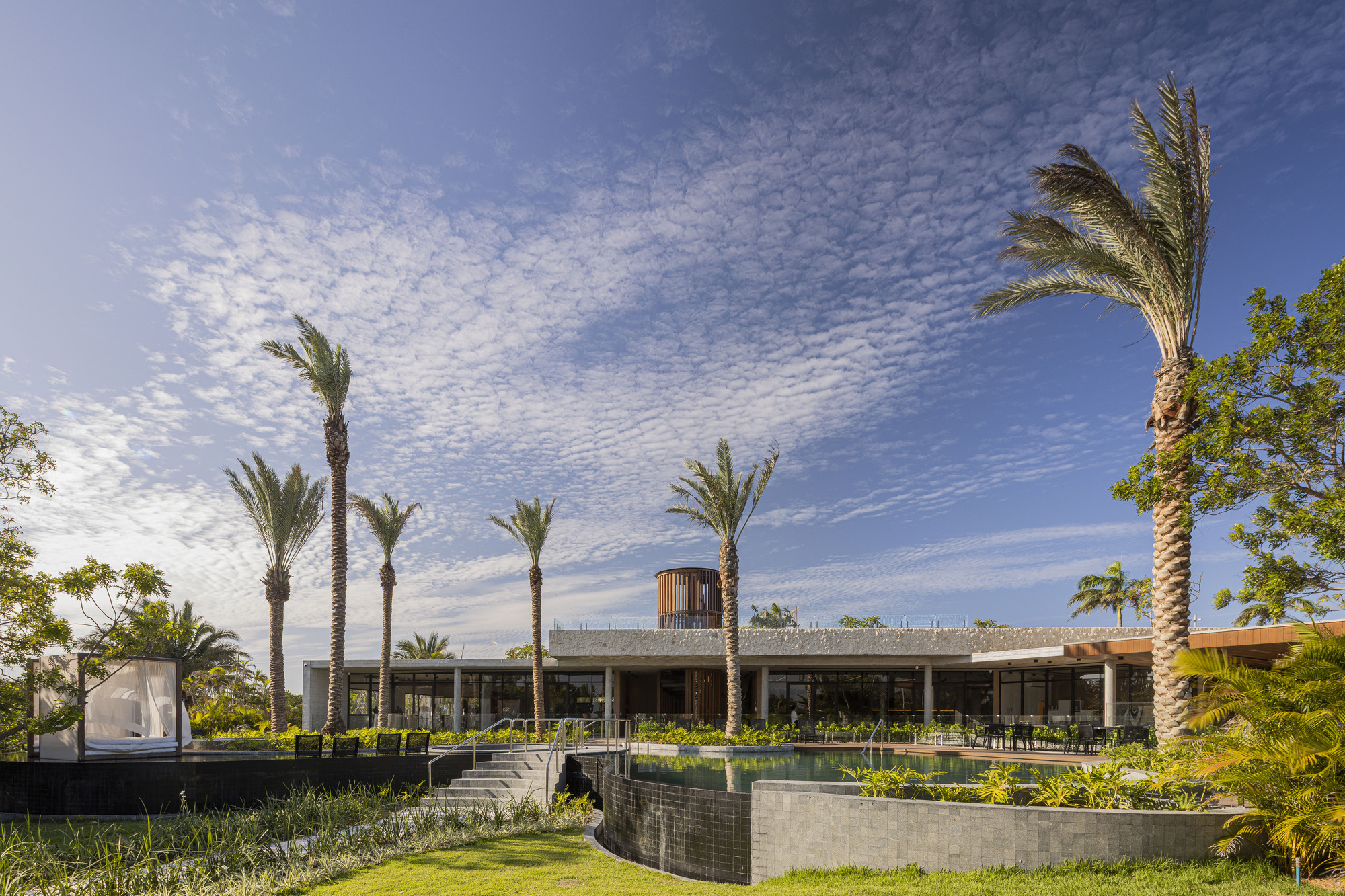 Low concrete pavilion with horizontal roof slab and glazed walls set among palm trees and terraced landscape beds