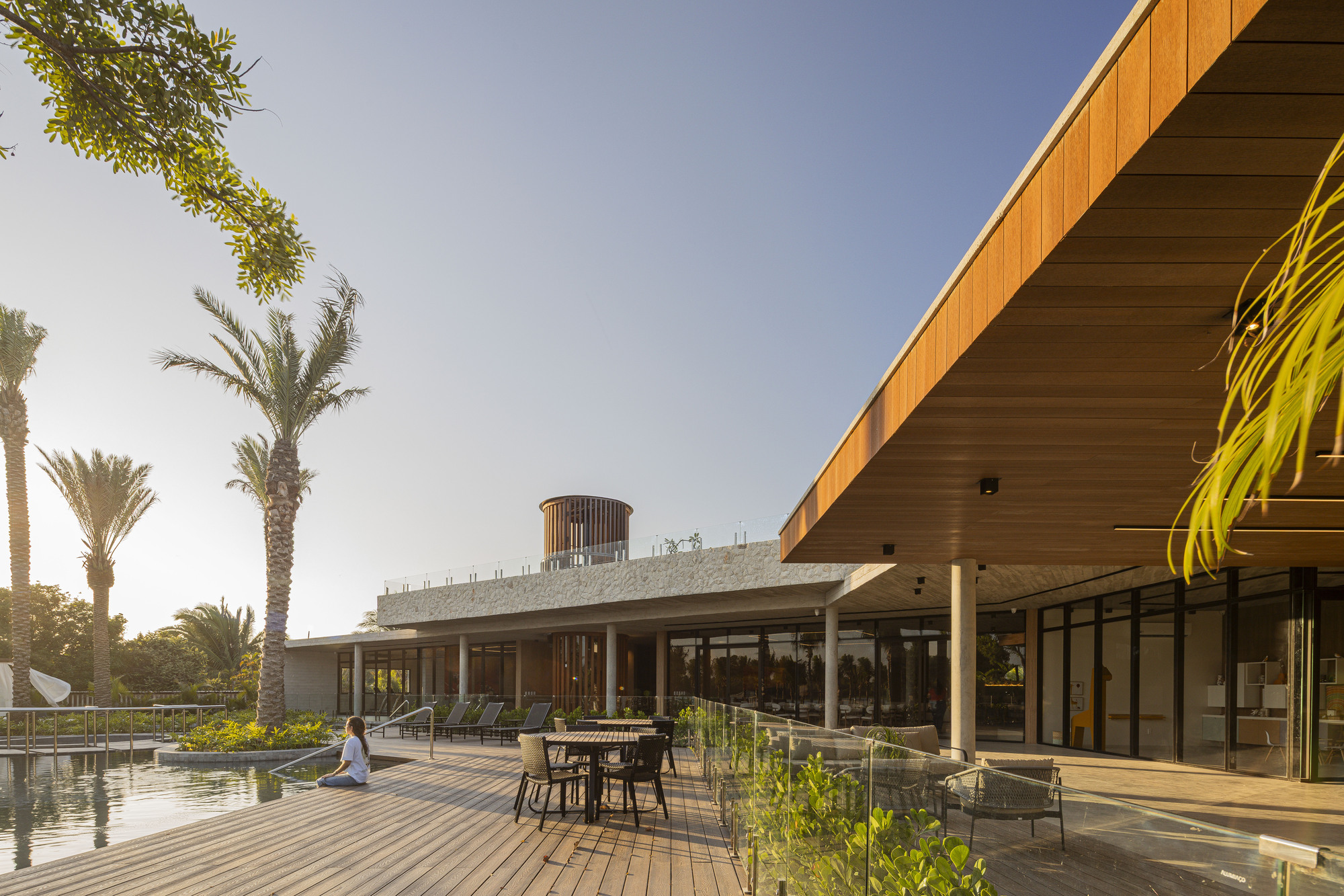 Timber-clad roof overhang and concrete terrace with pool and outdoor furniture at sunset
