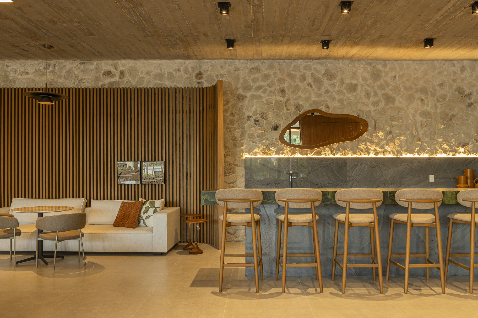 Bar counter with timber stools beneath a river stone wall and board-formed concrete ceiling