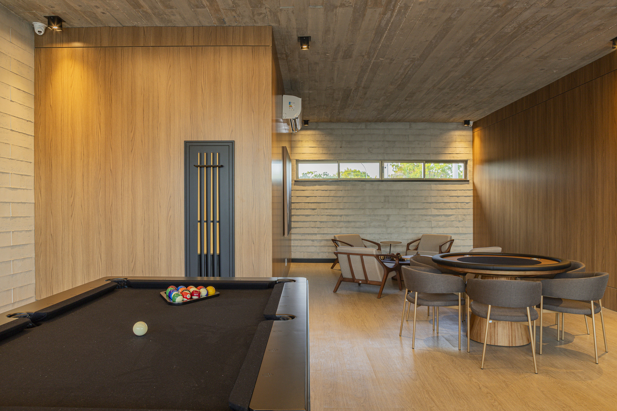 Recreation room with pool table and card table beneath exposed concrete ceilings and horizontal windows
