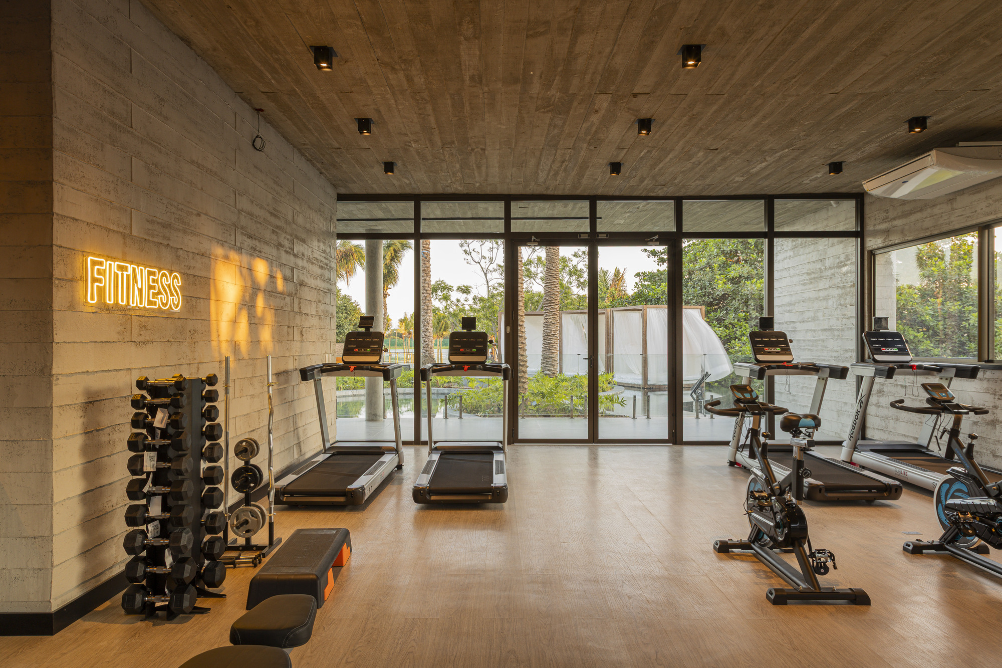 Fitness room with treadmills and equipment beneath board-formed concrete ceiling overlooking vegetation through glazed walls