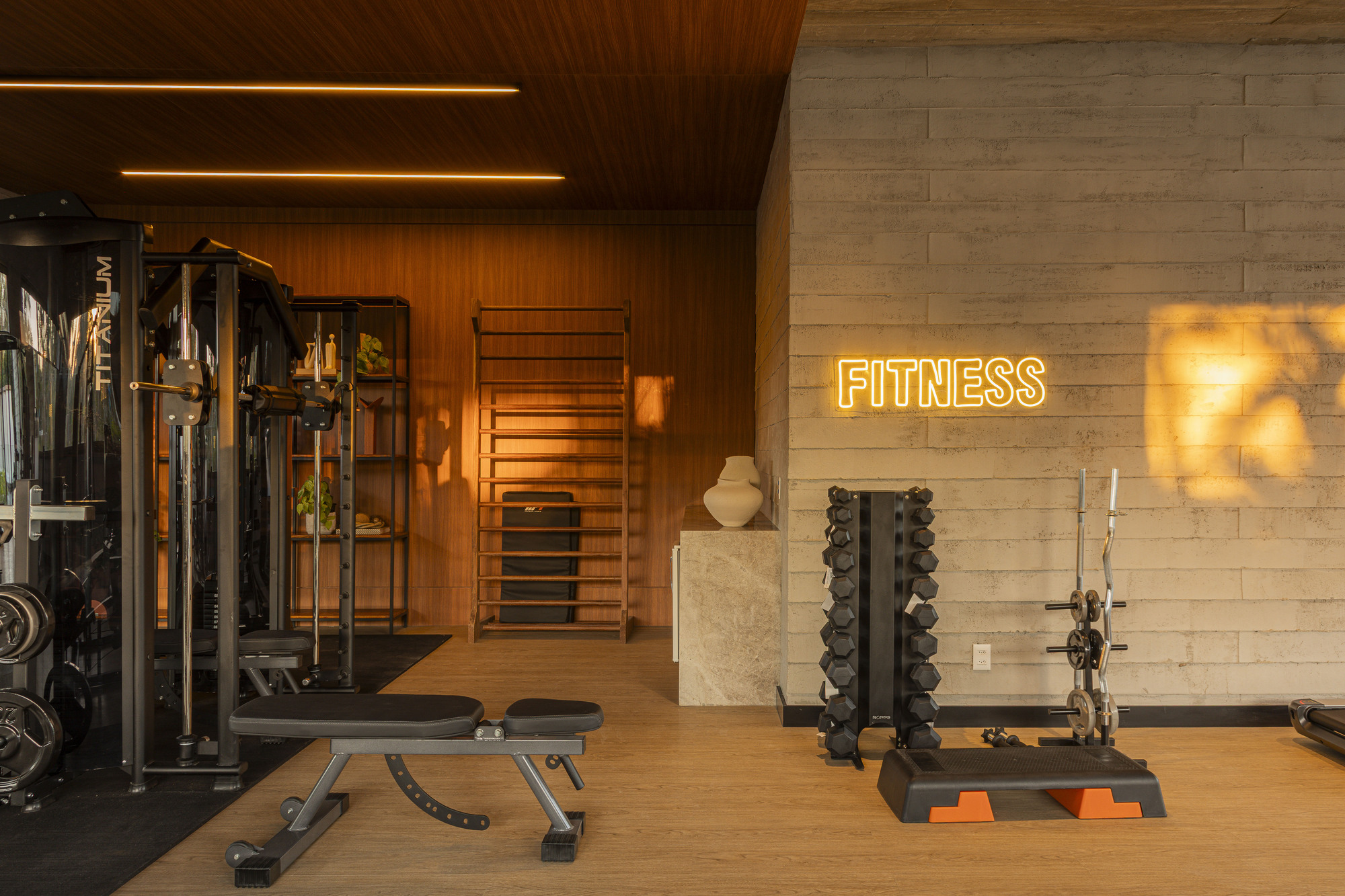 Corner of fitness room with illuminated neon signage and weight racks against concrete and timber walls
