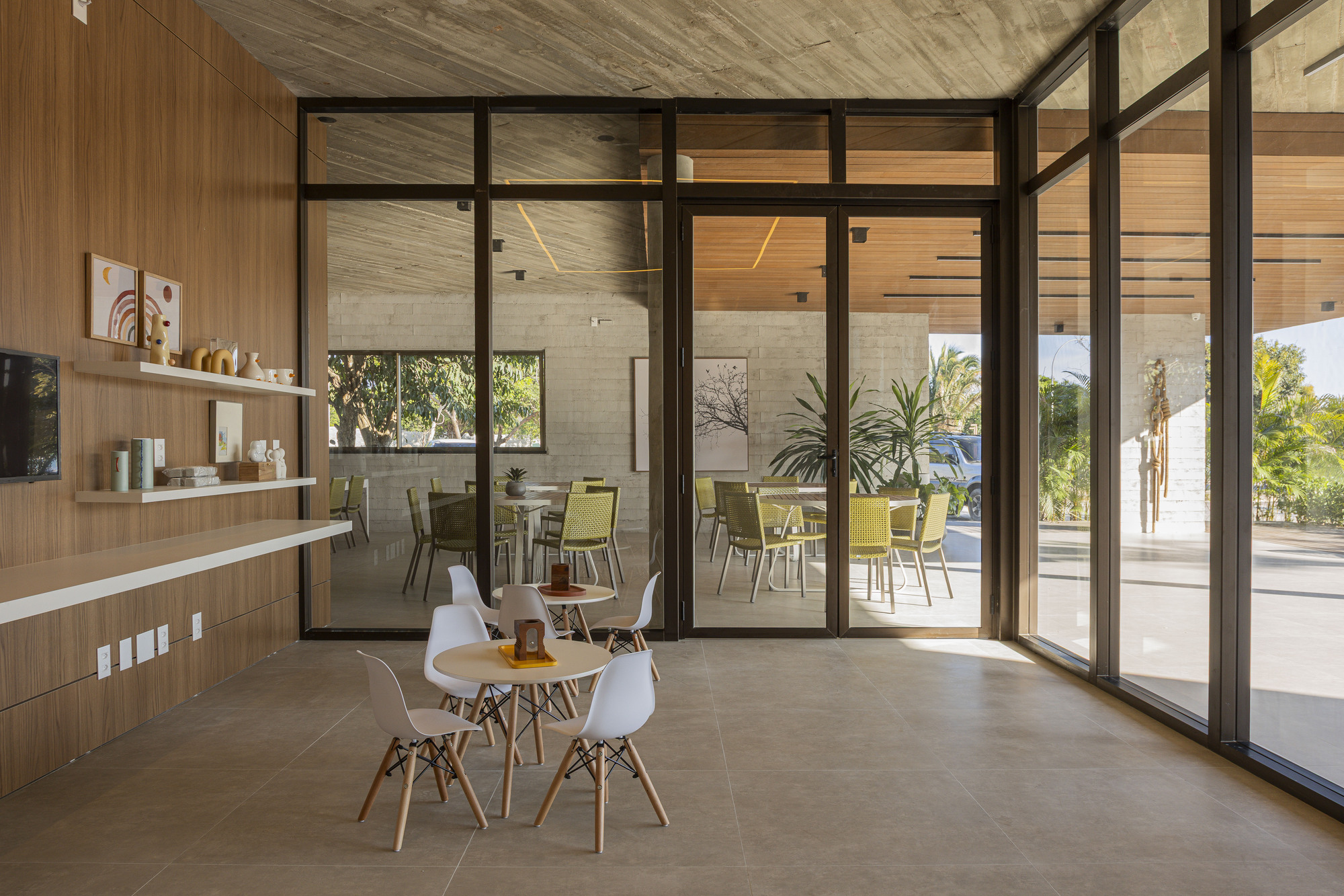 Interior dining area with steel-framed glass doors opening to poolside terrace with palm trees beyond