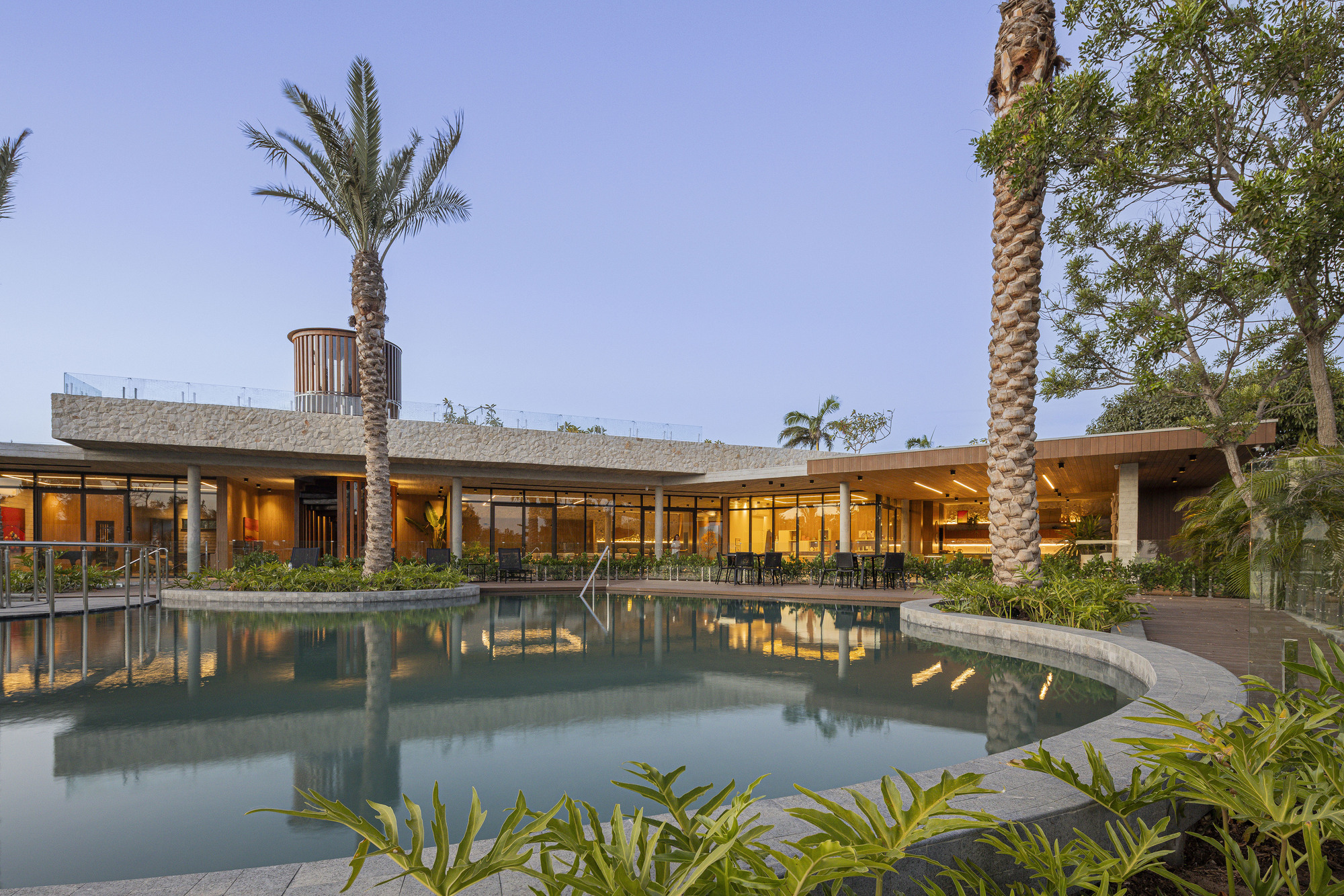 Curved pool reflecting the low-slung glazed facade framed by palm trees at twilight
