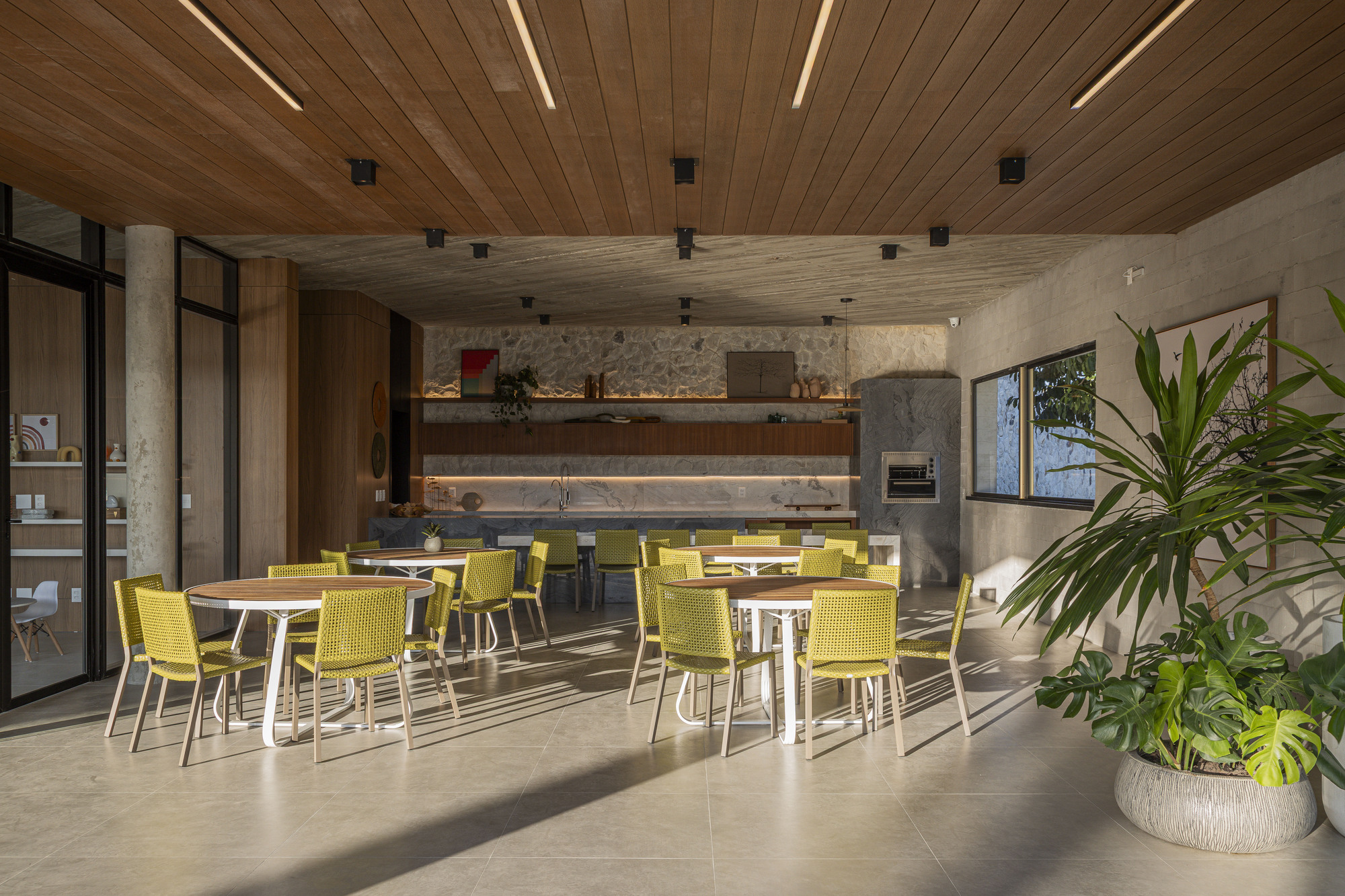 Open dining area with yellow chairs under slatted timber ceiling and concrete service wall