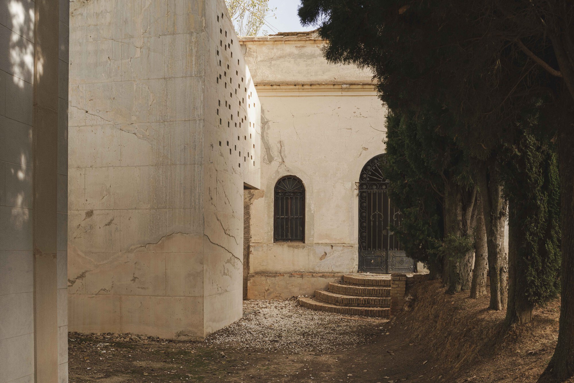 Perforated concrete tower beside stone steps leading to arched doorways framed by tall trees