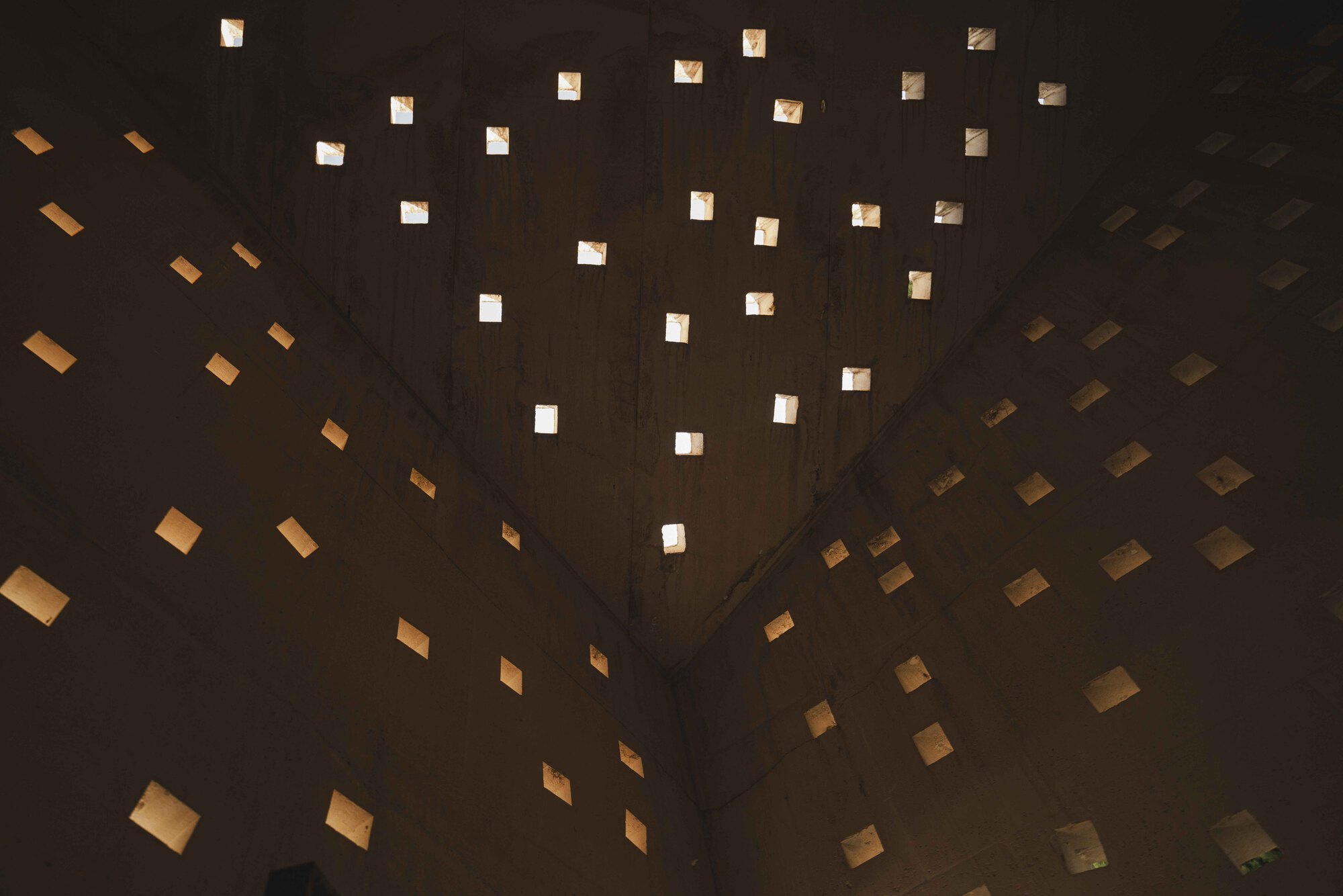 Upward interior view of scattered square openings puncturing the concrete ceiling plane