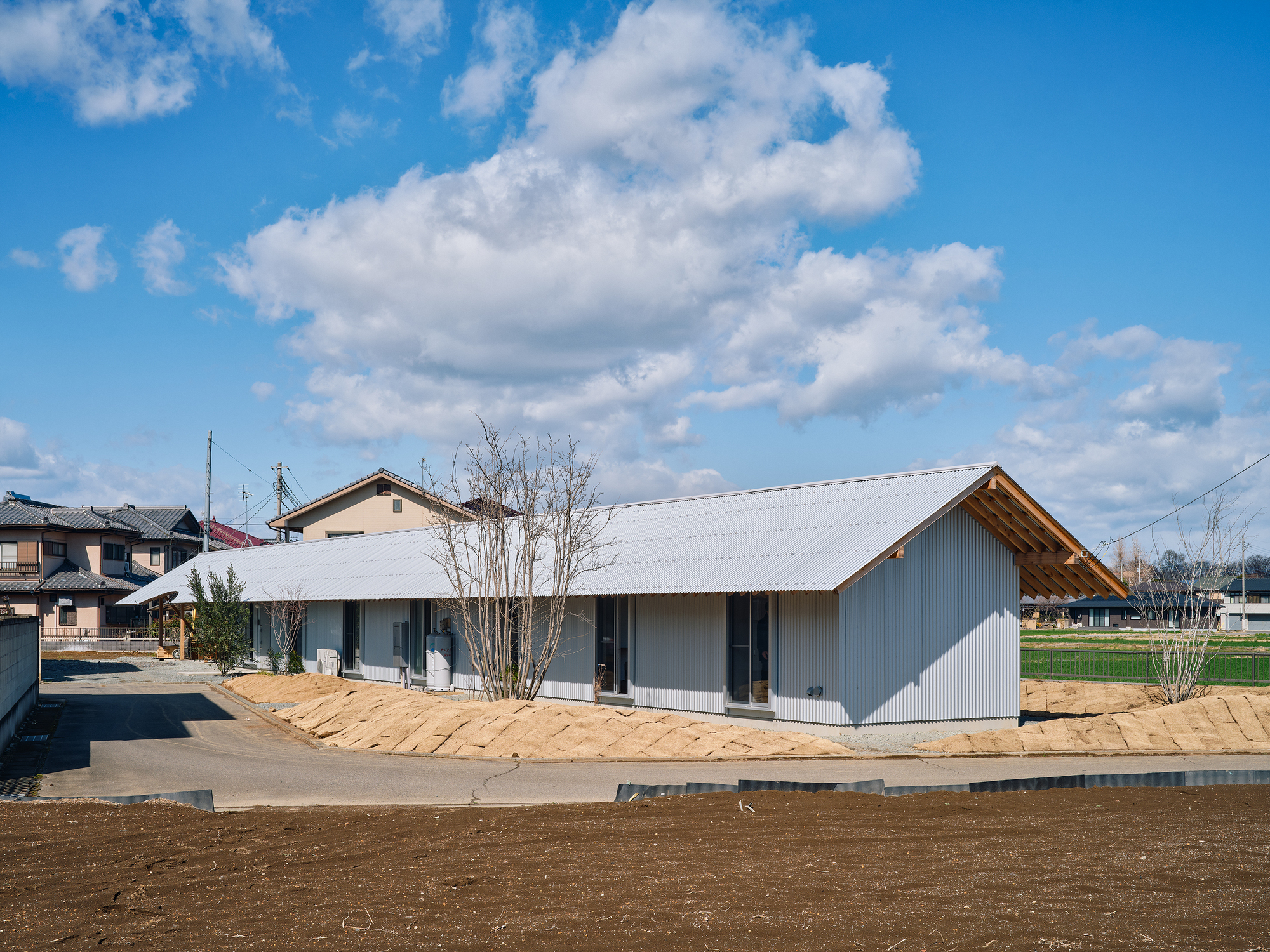 Street view of the corrugated metal volume with gabled roof and timber eaves in a neighborhood setting