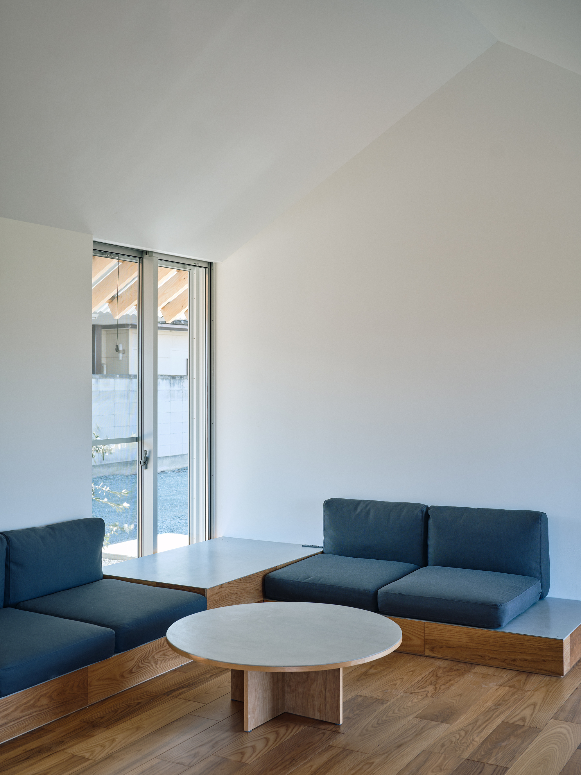 Interior seating area with built-in blue cushioned benches and low round table on timber flooring