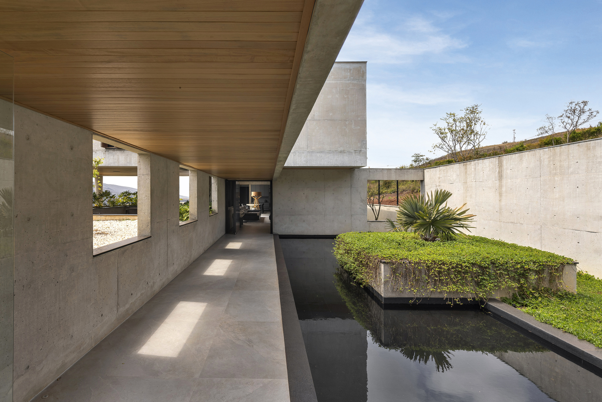 Covered walkway alongside a reflecting pool with timber ceiling and planted courtyard walls