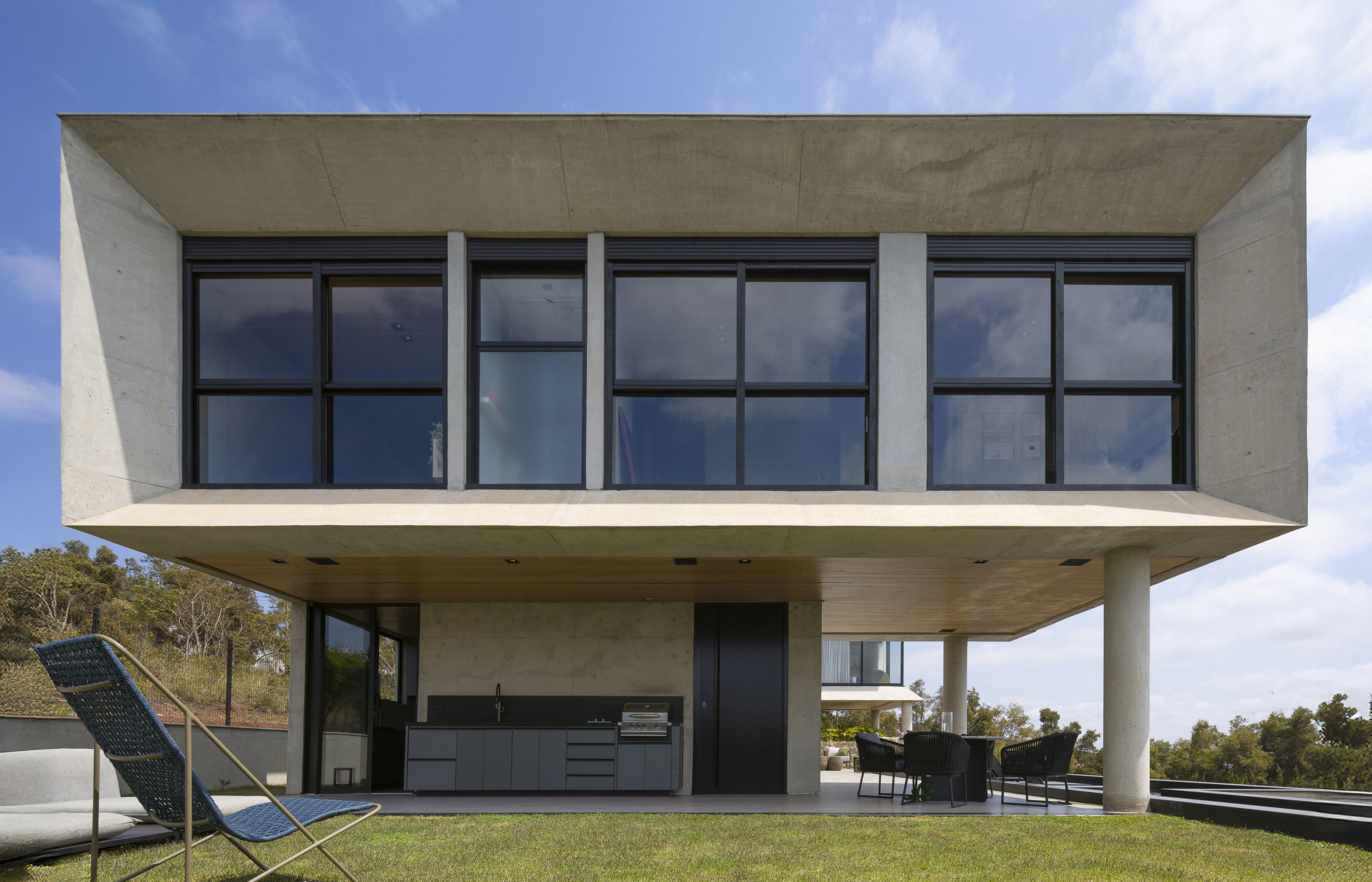 Cantilevered concrete upper volume with grid windows above a covered outdoor kitchen
