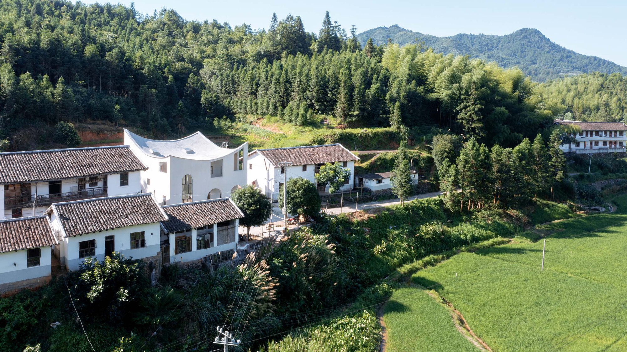 Aerial view of white-walled courtyard houses with tiled roofs nestled among forested hills and terraced farmland