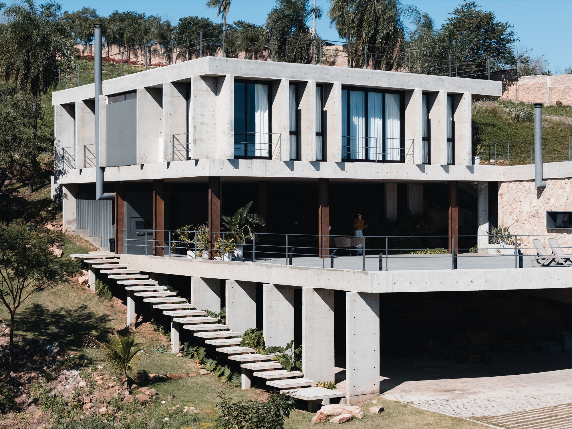 Concrete stairway ascending the hillside alongside the piloti and cantilevered upper volume