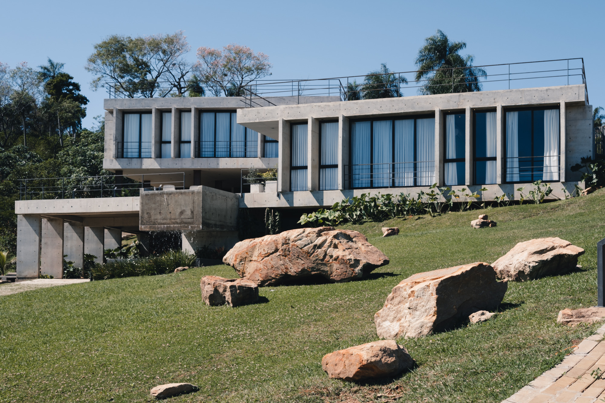 Cantilevered concrete facade with rhythmic vertical fins above a grassy slope scattered with large boulders