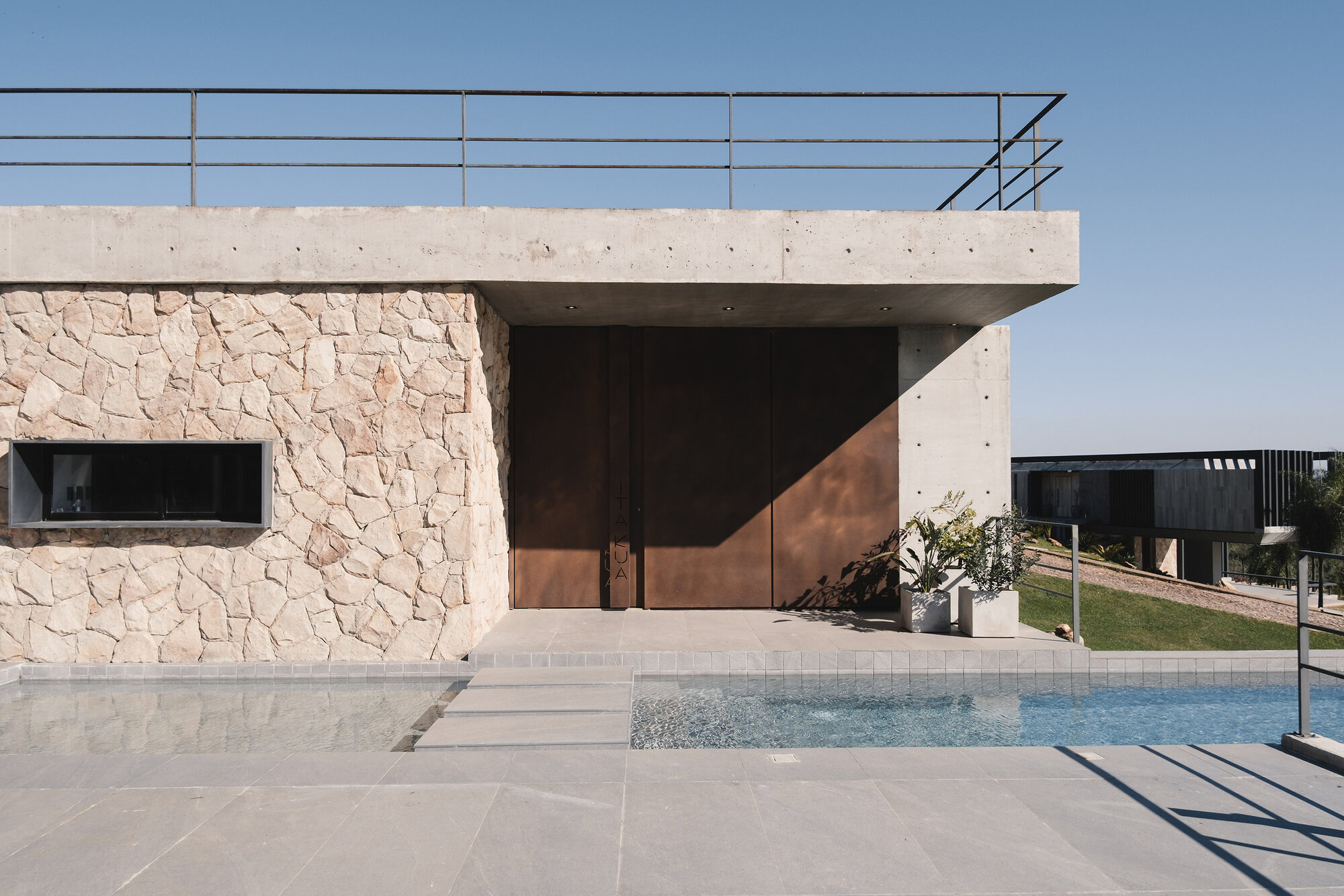 Entry facade with stone cladding, timber pivot door, concrete canopy, and adjacent pool deck
