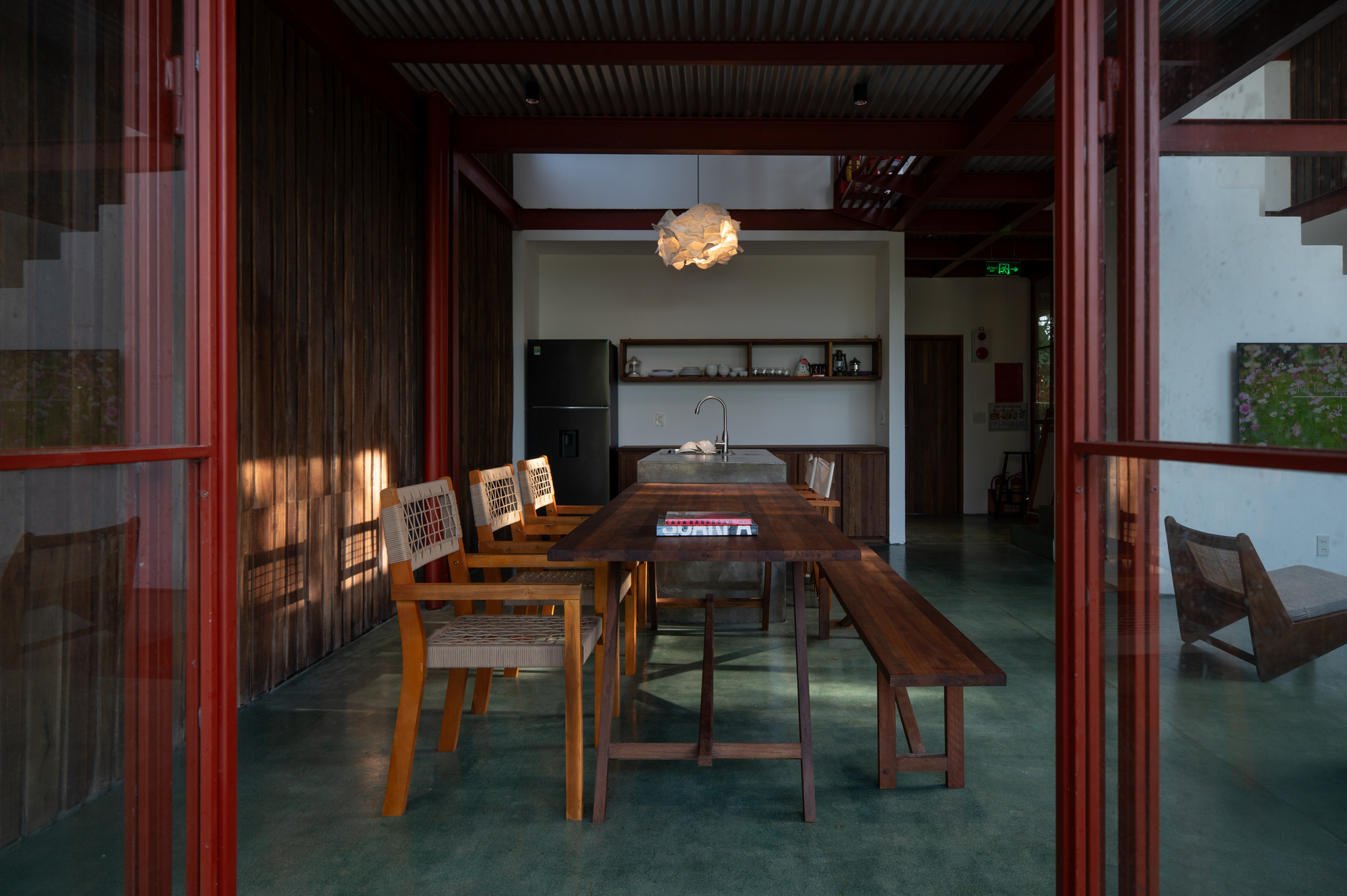 Living space looking through red framed glass doors toward kitchen alcove with pendant light overhead