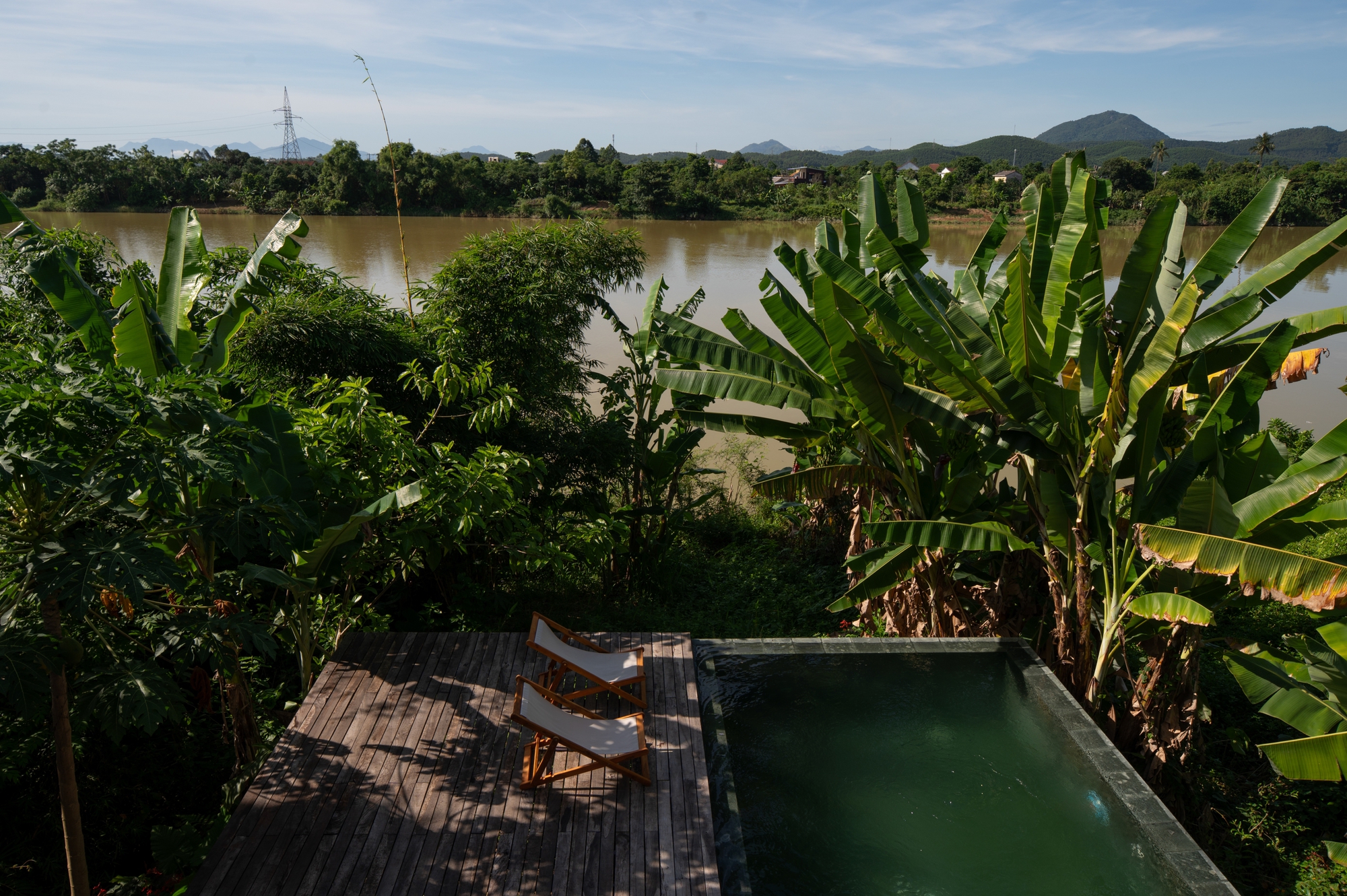 Timber deck terrace with pool and lounge chairs overlooking banana trees and a wide river