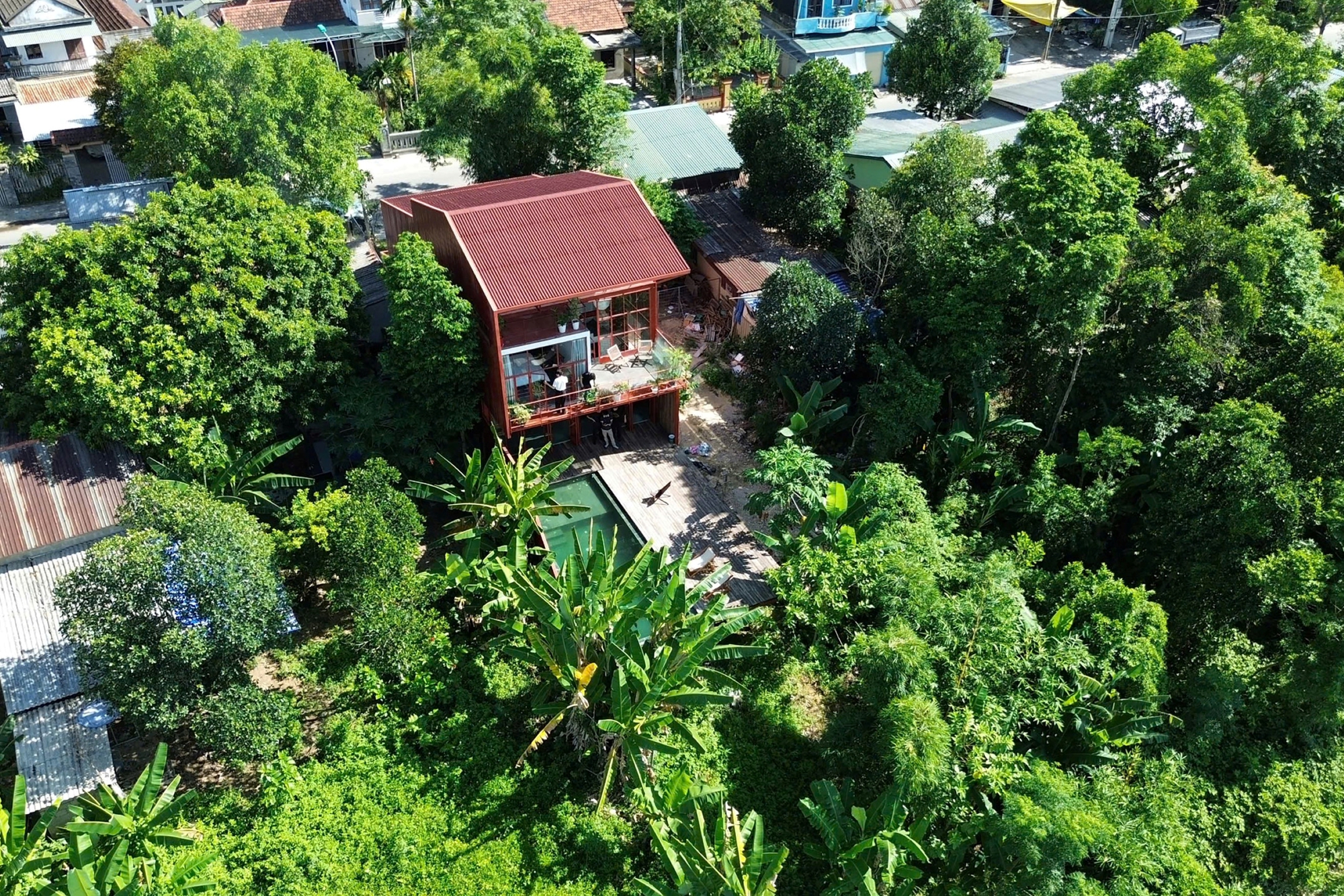 Aerial view of the red corrugated metal roof among dense tree canopy and neighboring houses